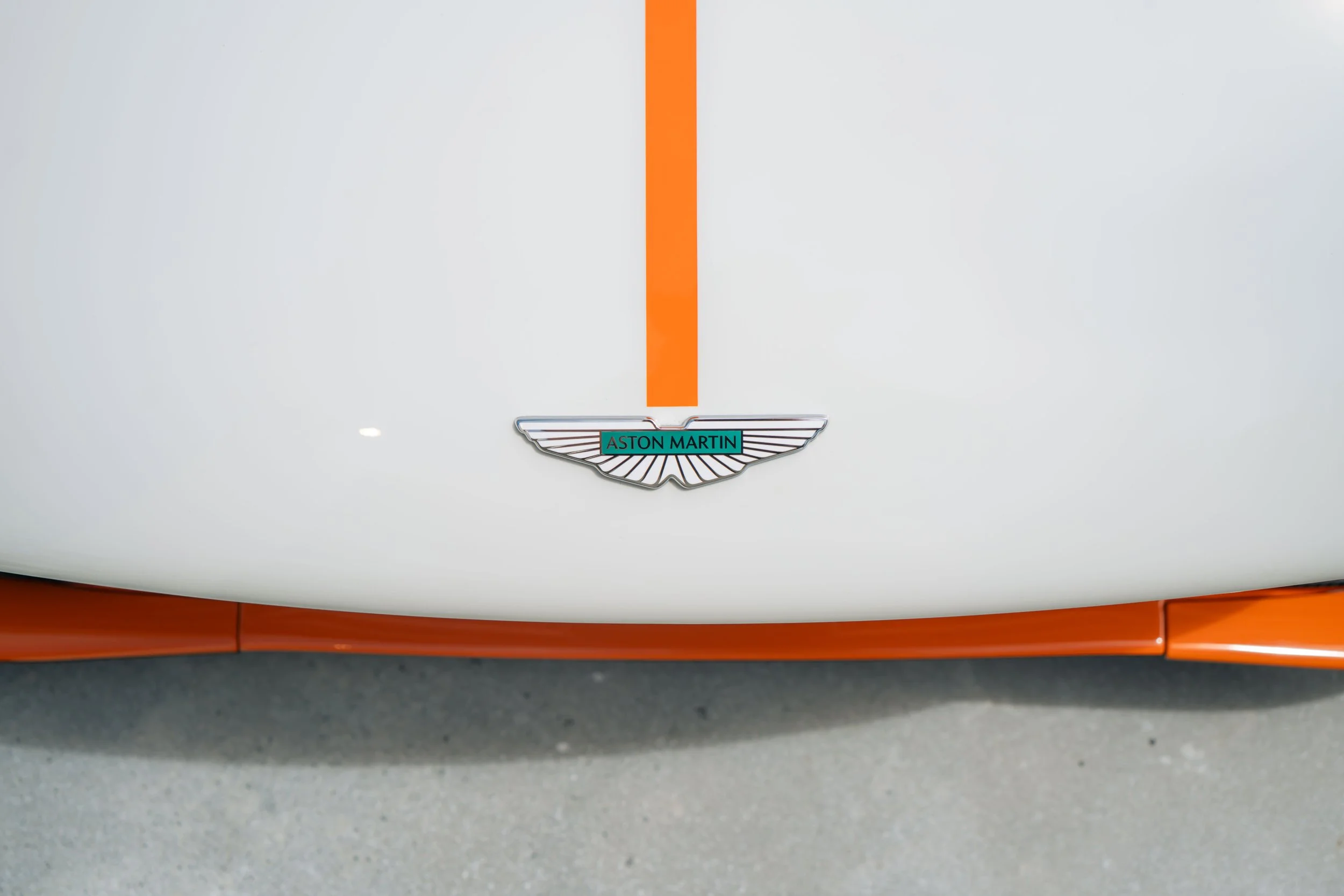 Close-up of a white car hood with an orange stripe and the Aston Martin logo.