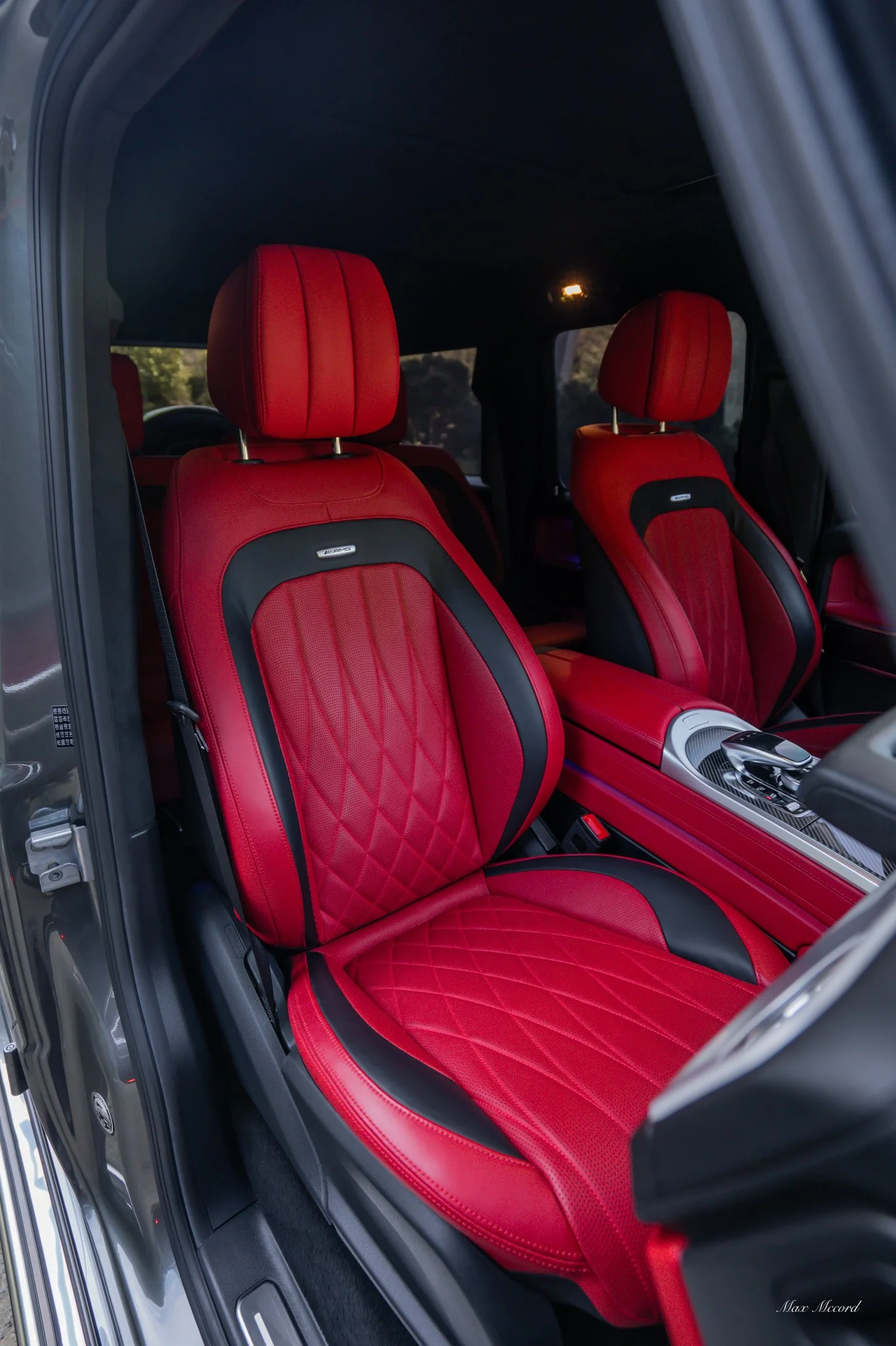 Inside view of a luxury vehicle featuring red leather seats with black accents and diamond stitching, sharp headrests, and a sleek center console.