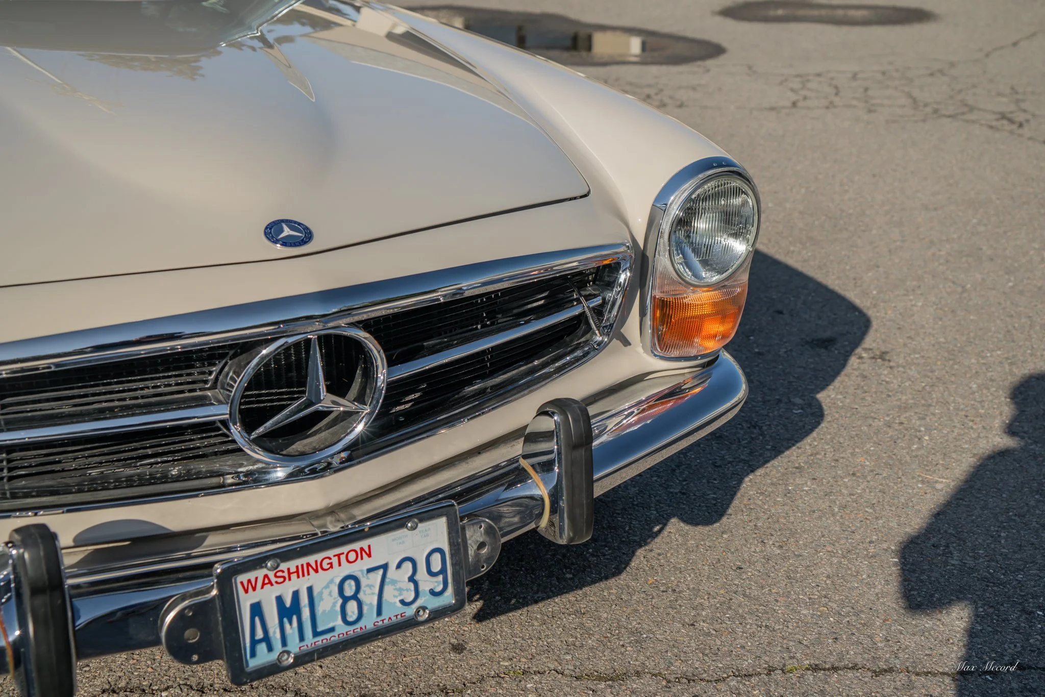 Close-up of the front part of a vintage white Mercedes-Benz car with a Washington license plate, chrome grille, and round headlights, cast in sunlight on a parking lot.