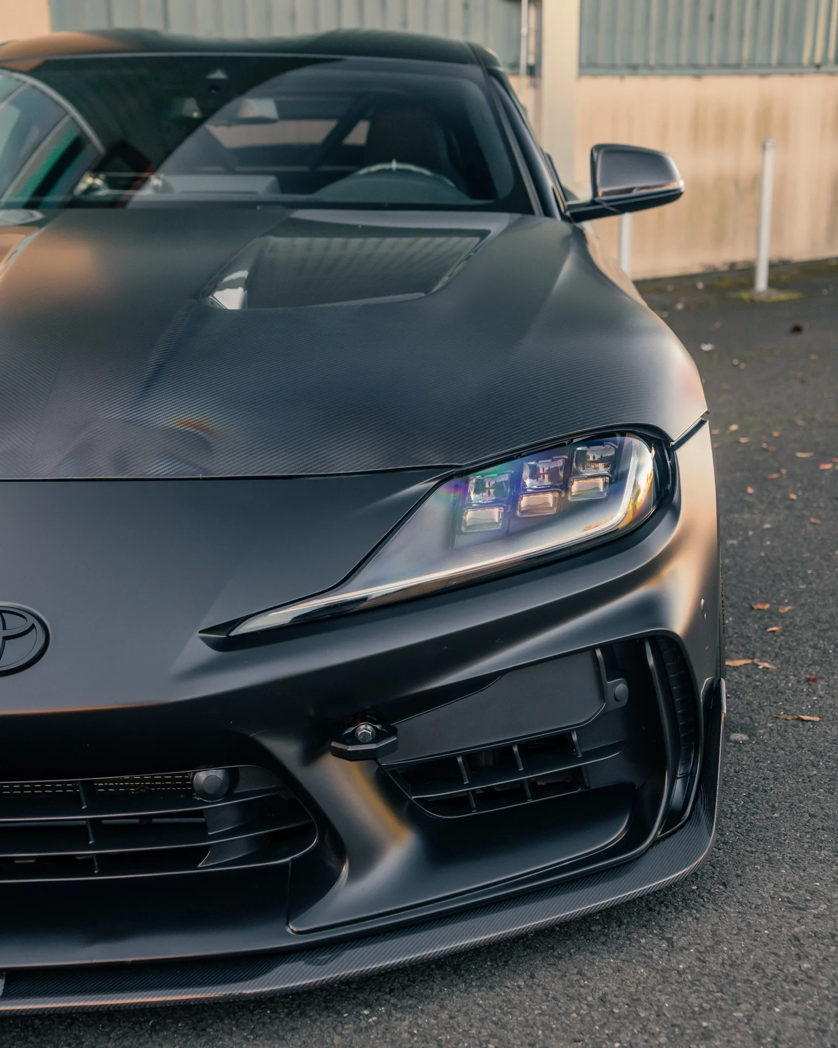 Close-up of the front of a matte black Toyota sports car with sleek design and carbon fiber accents