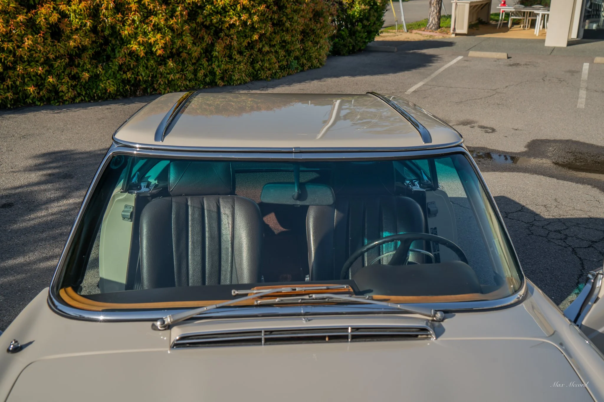 Top view of a vintage cream-colored car with black leather seats parked in a lot near greenery and a building.