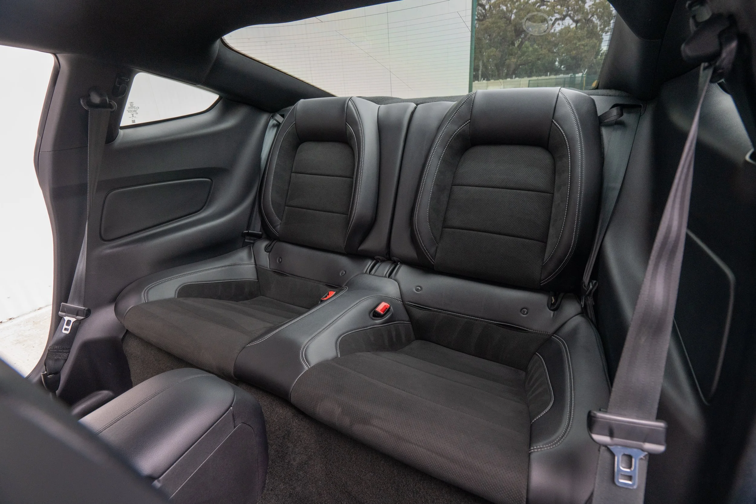 Rear seat of a black car interior with two separate seats and black seat belts.