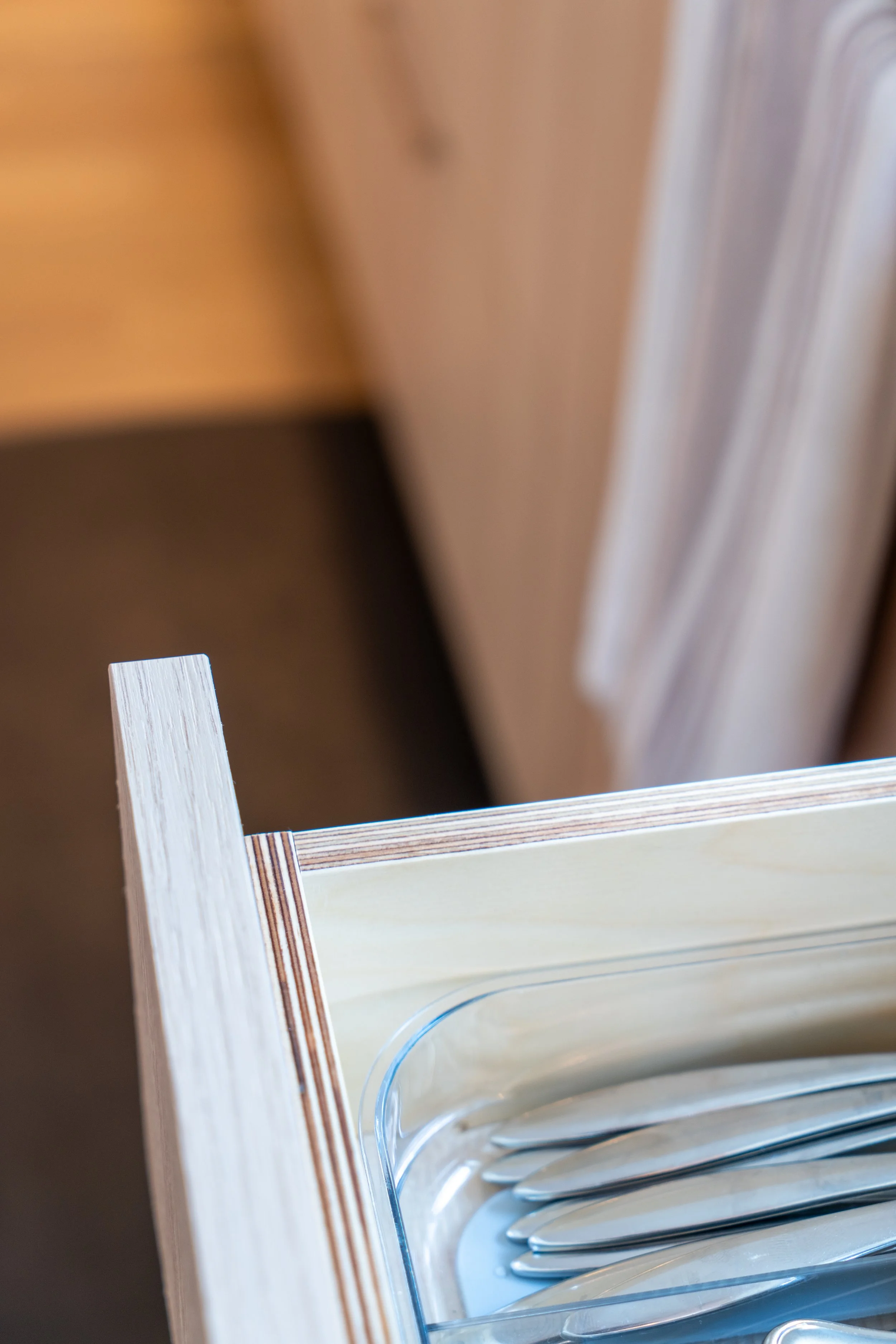 Close-up of a wooden drawer containing silverware in a kitchen.