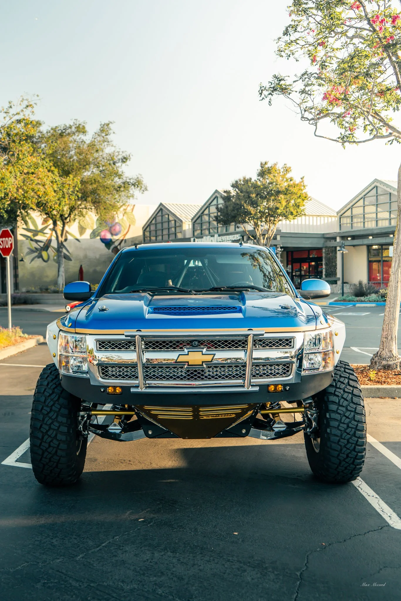 A black and yellow off-road Chevrolet truck parked in a parking lot with trees and shopping centers in the background.
