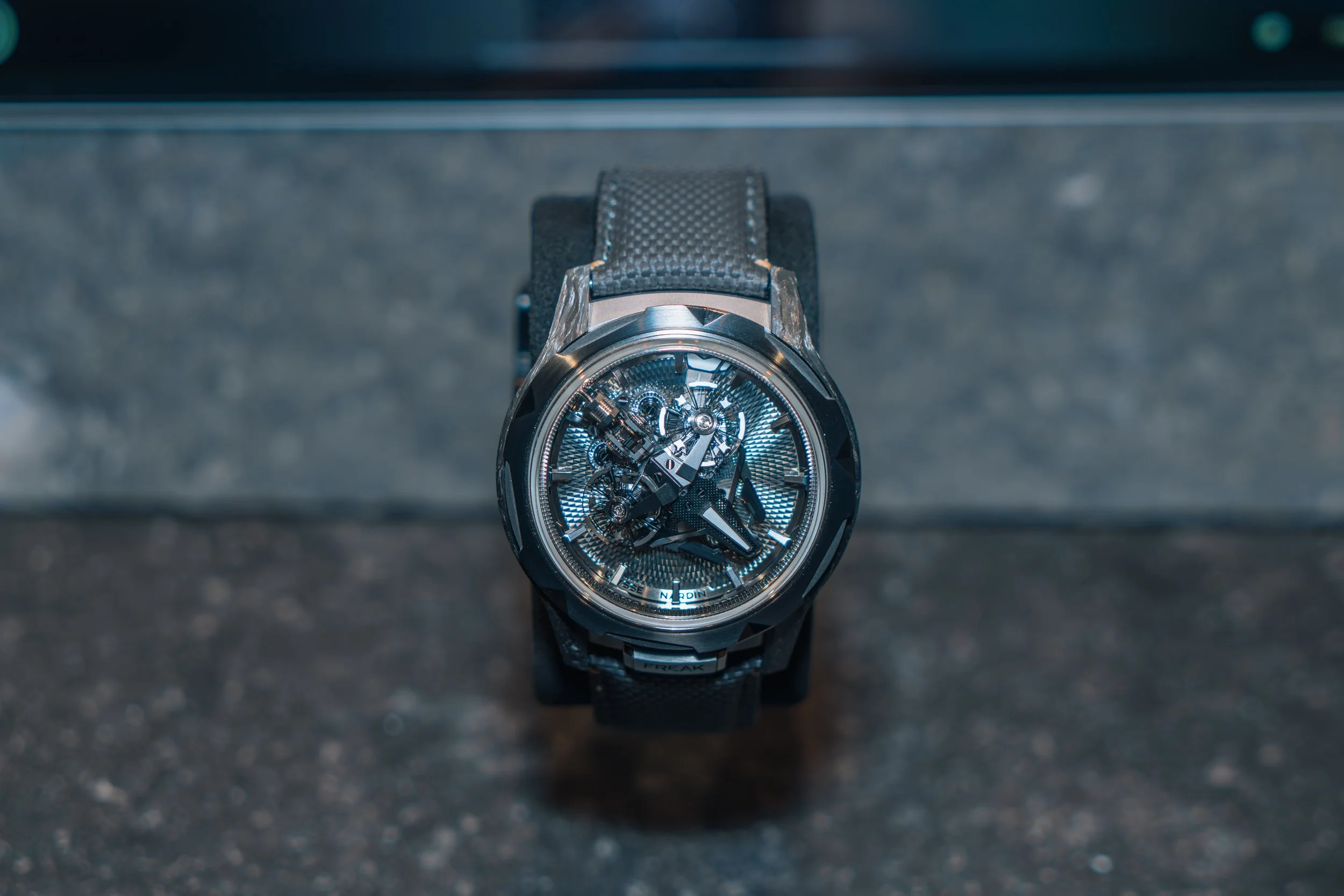A luxury wristwatch with a skeleton dial displaying the internal mechanics, mounted on a black textured strap.
