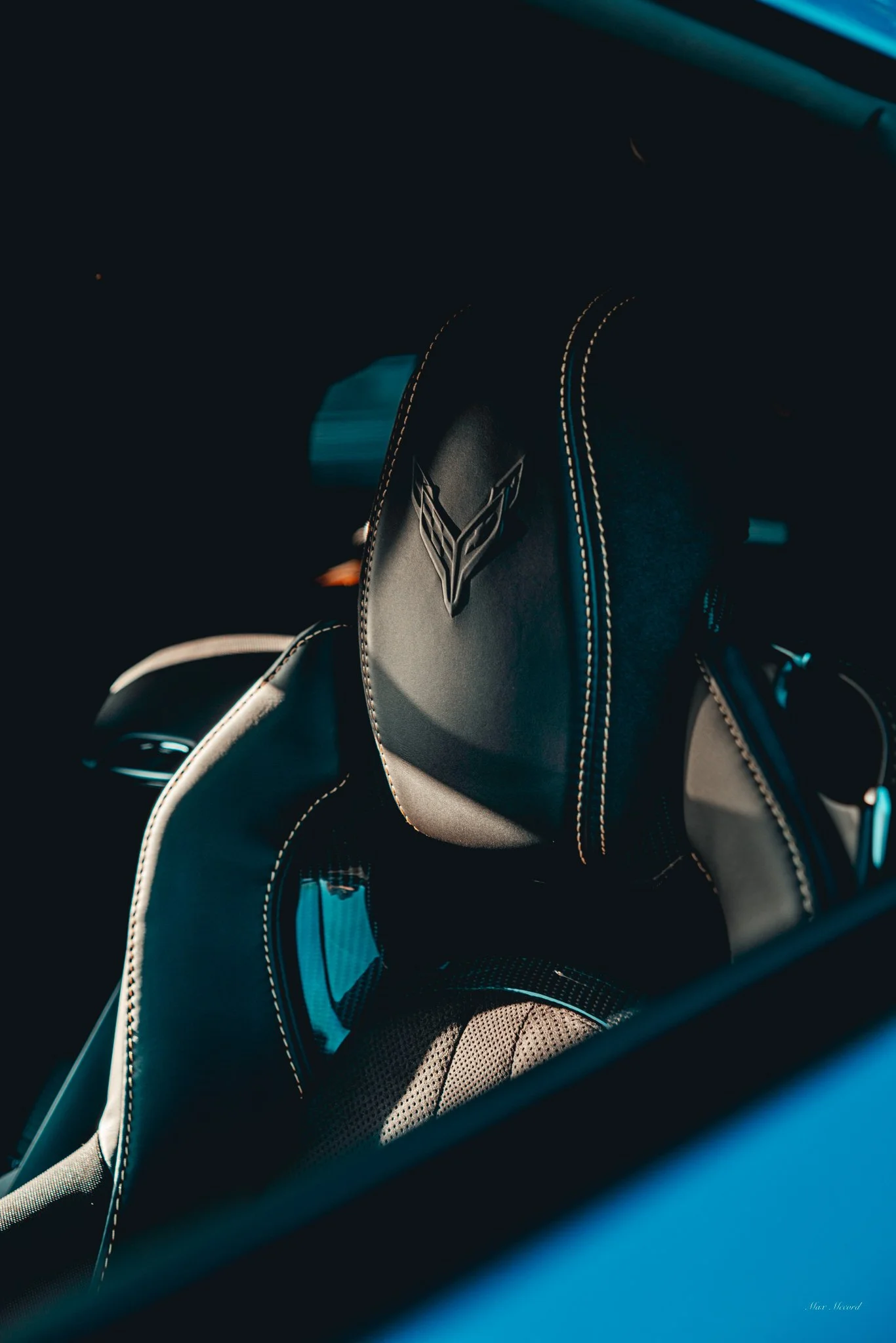 Close-up of a black car seat with the Chevrolet Corvette logo and beige stitching visible.