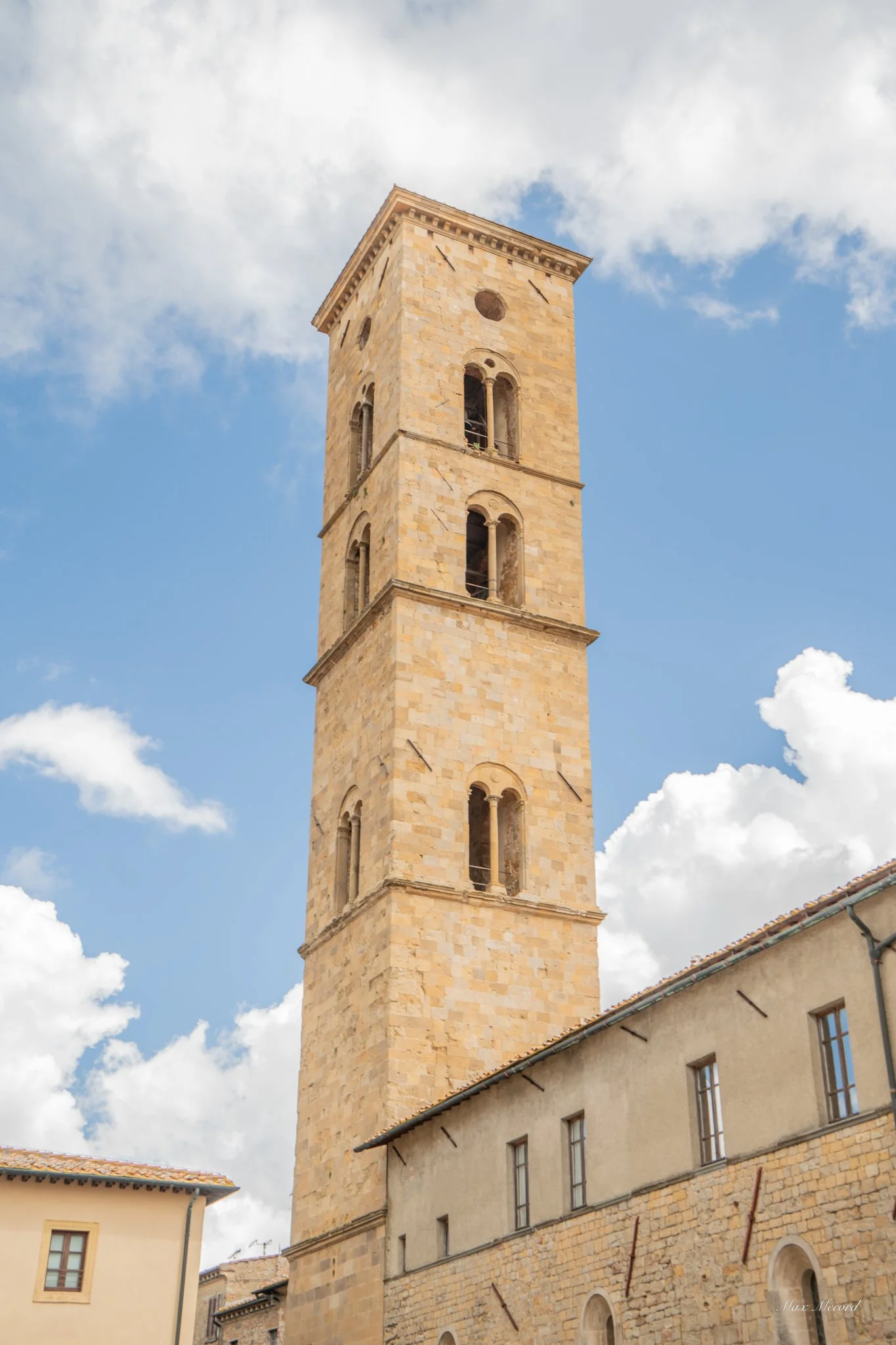 A tall stone bell tower with arched windows set against a partly cloudy sky.