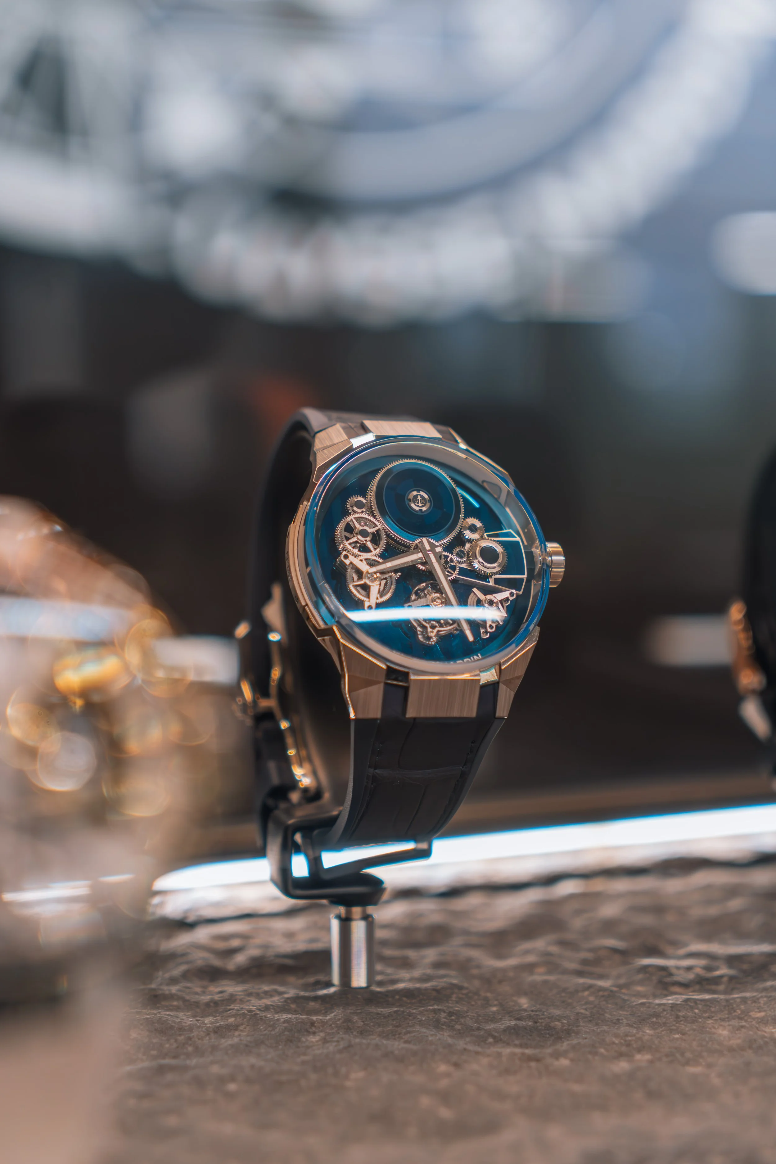 Close-up of a luxury wristwatch with a mechanical skeleton dial, black strap, and metal case displayed on a stand.