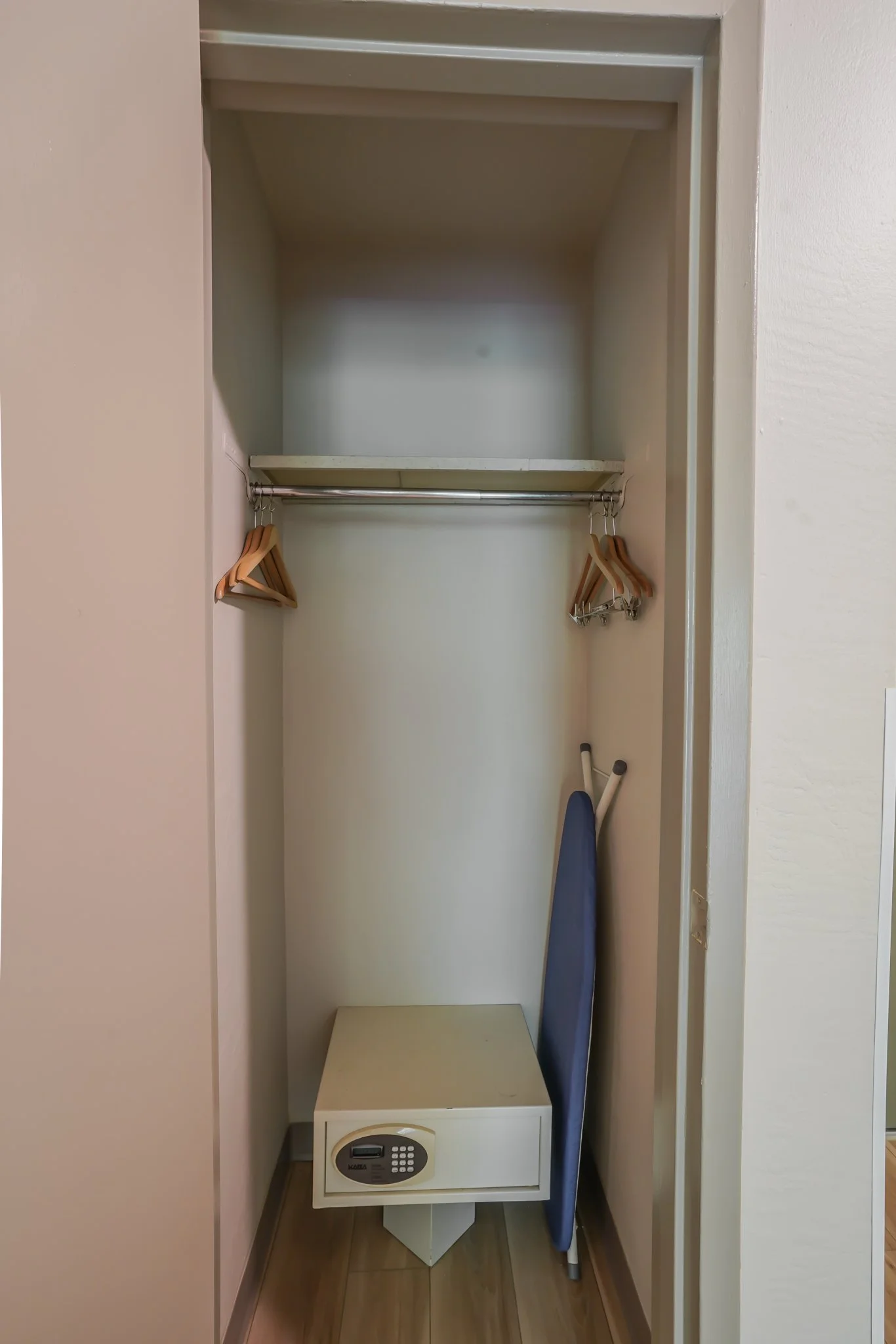 Empty closet with a small safe, an ironing board, and a few wooden hangers.