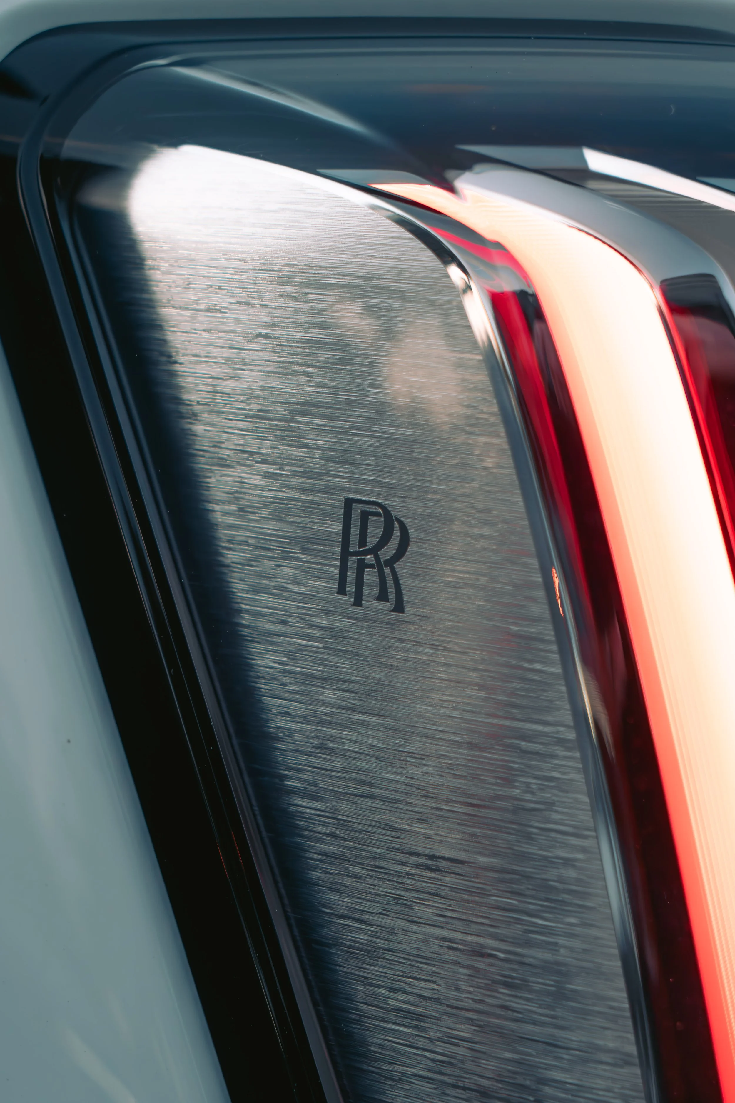 Close-up of a car's rear window with a black 'RR' logo and red tail light.