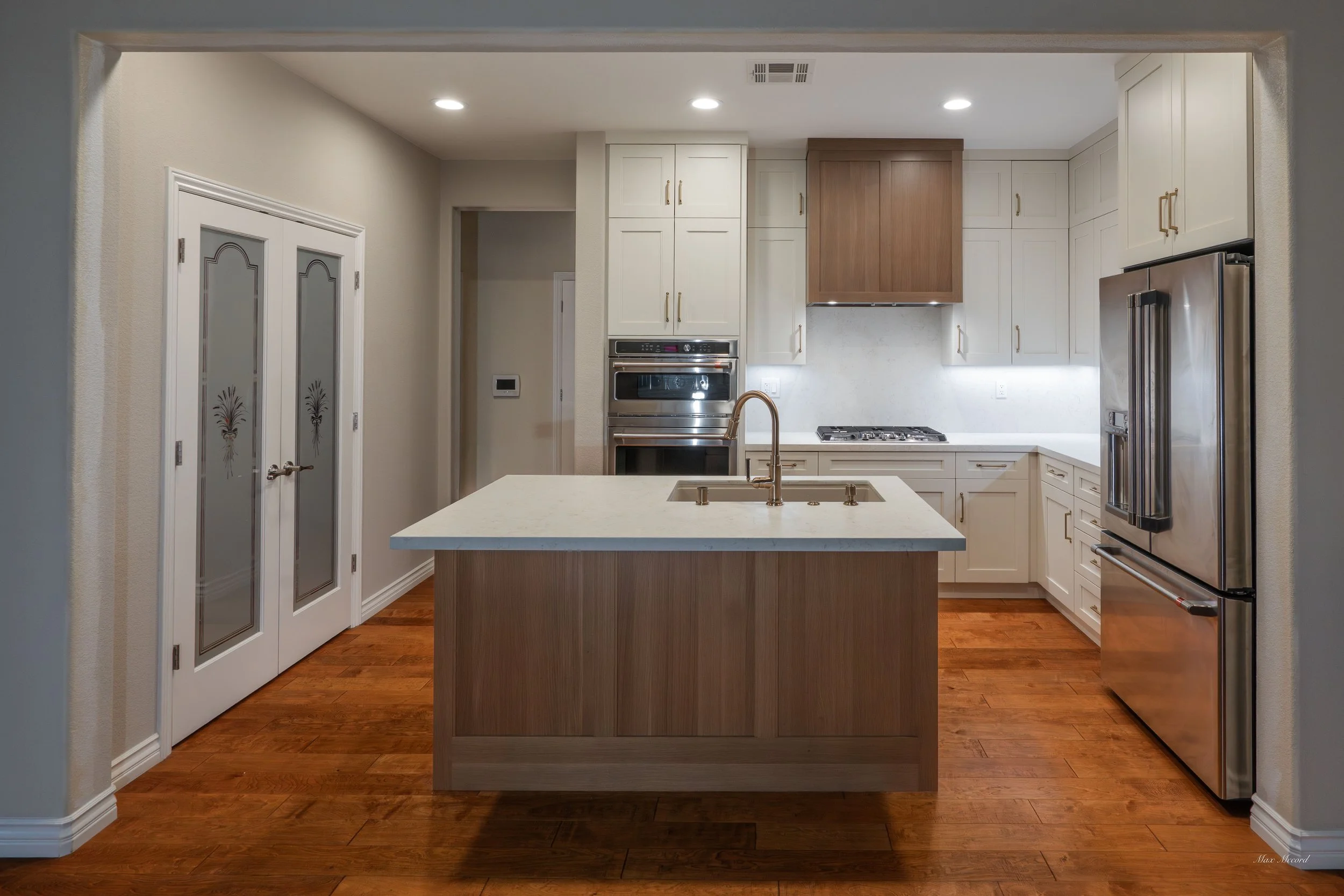 Modern kitchen with white cabinets, stainless steel appliances, an island with a sink, and hardwood floors.
