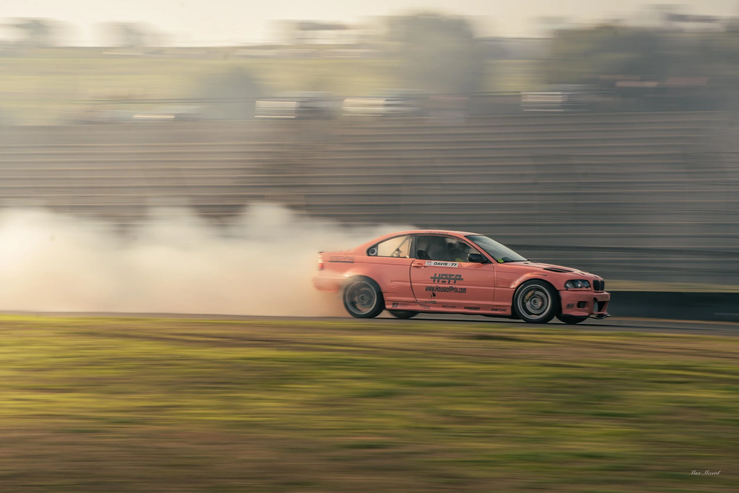 Pink race car drifting on a track, creating smoke behind it, with blurred background.