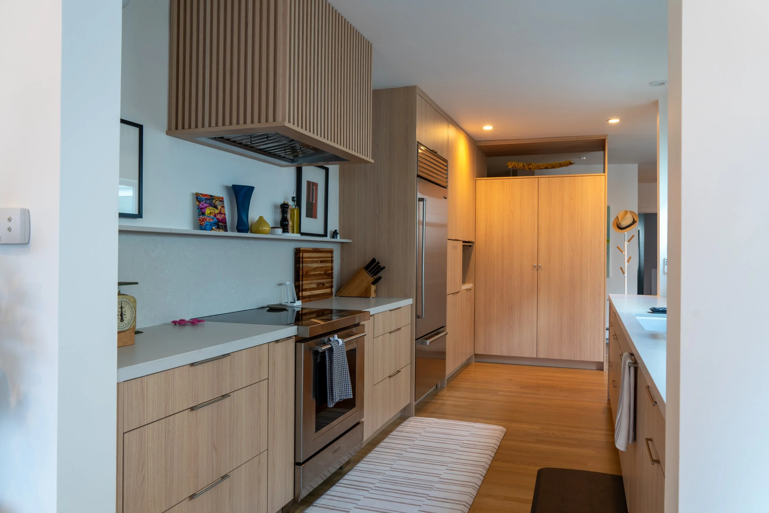Modern kitchen with wooden cabinets, stainless steel appliances, and striped rug on wooden floor.