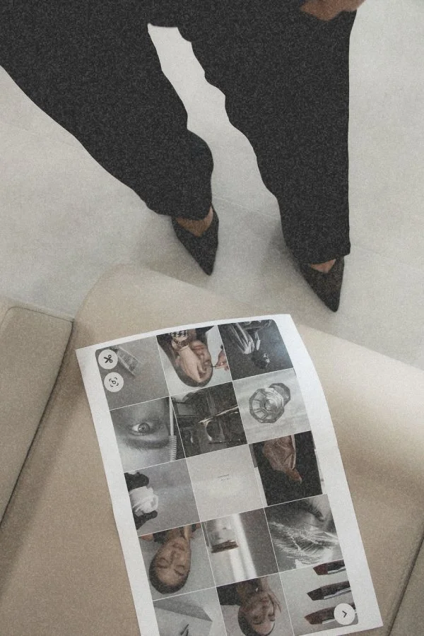 Person in black pants and pointed shoes standing near a collage of photos on a beige surface.