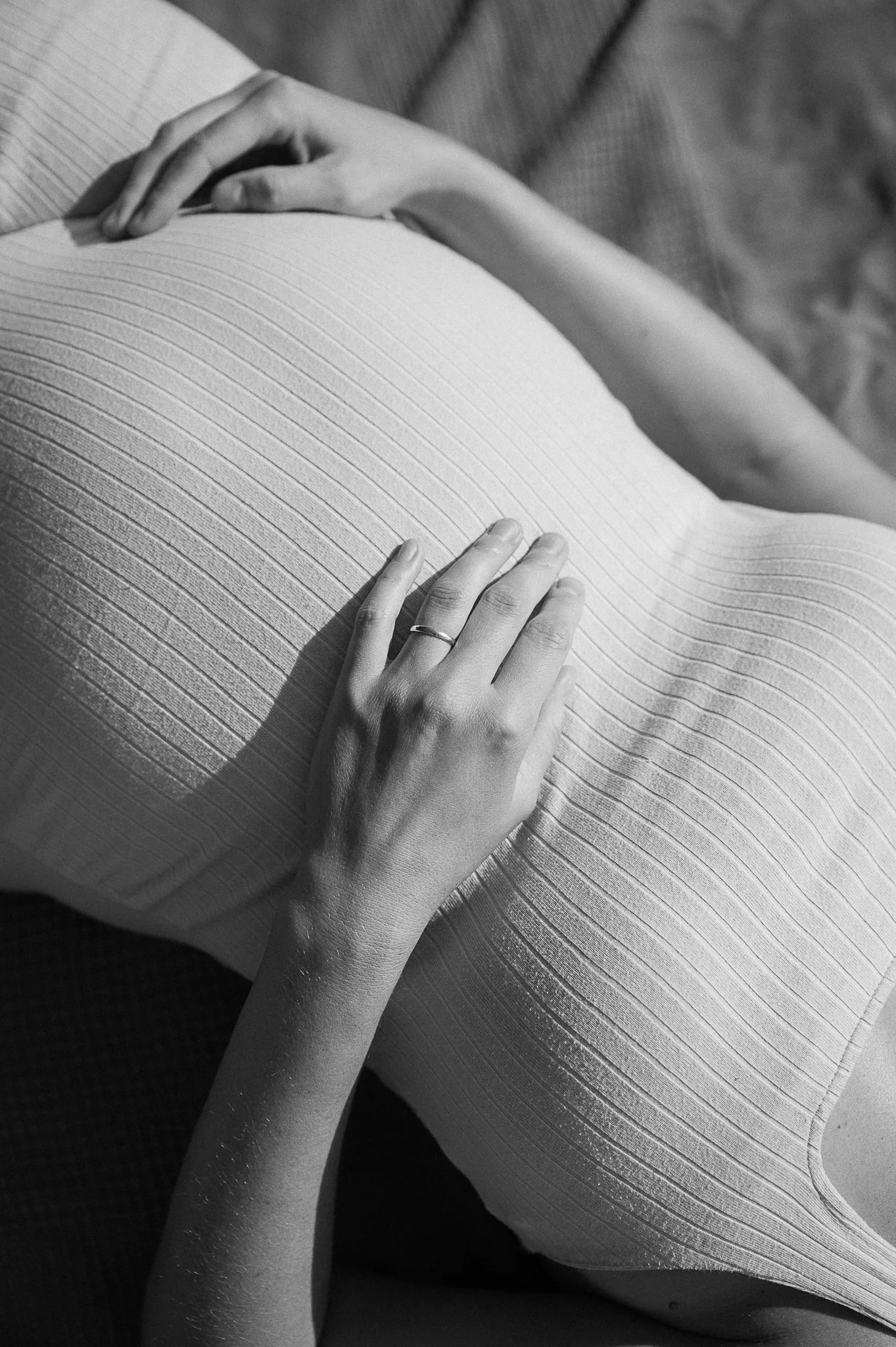 Schwarz-Weiß-Fotografie einer schwangeren jungen Frau, die ihren Babybauch streichelt.