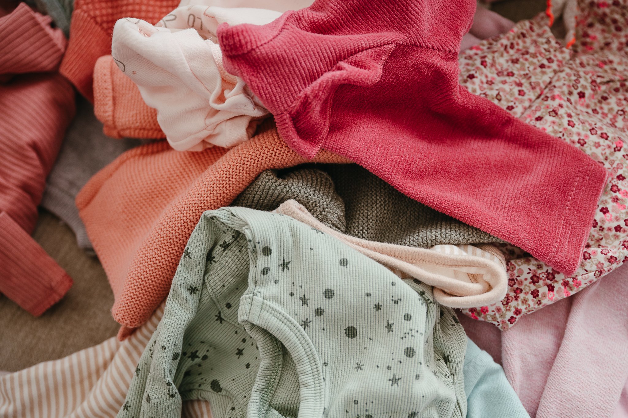Nahaufnahme eines Stapels bunter Babybekleidung mit Strickpullovern, Bodys und floralem Stoff.