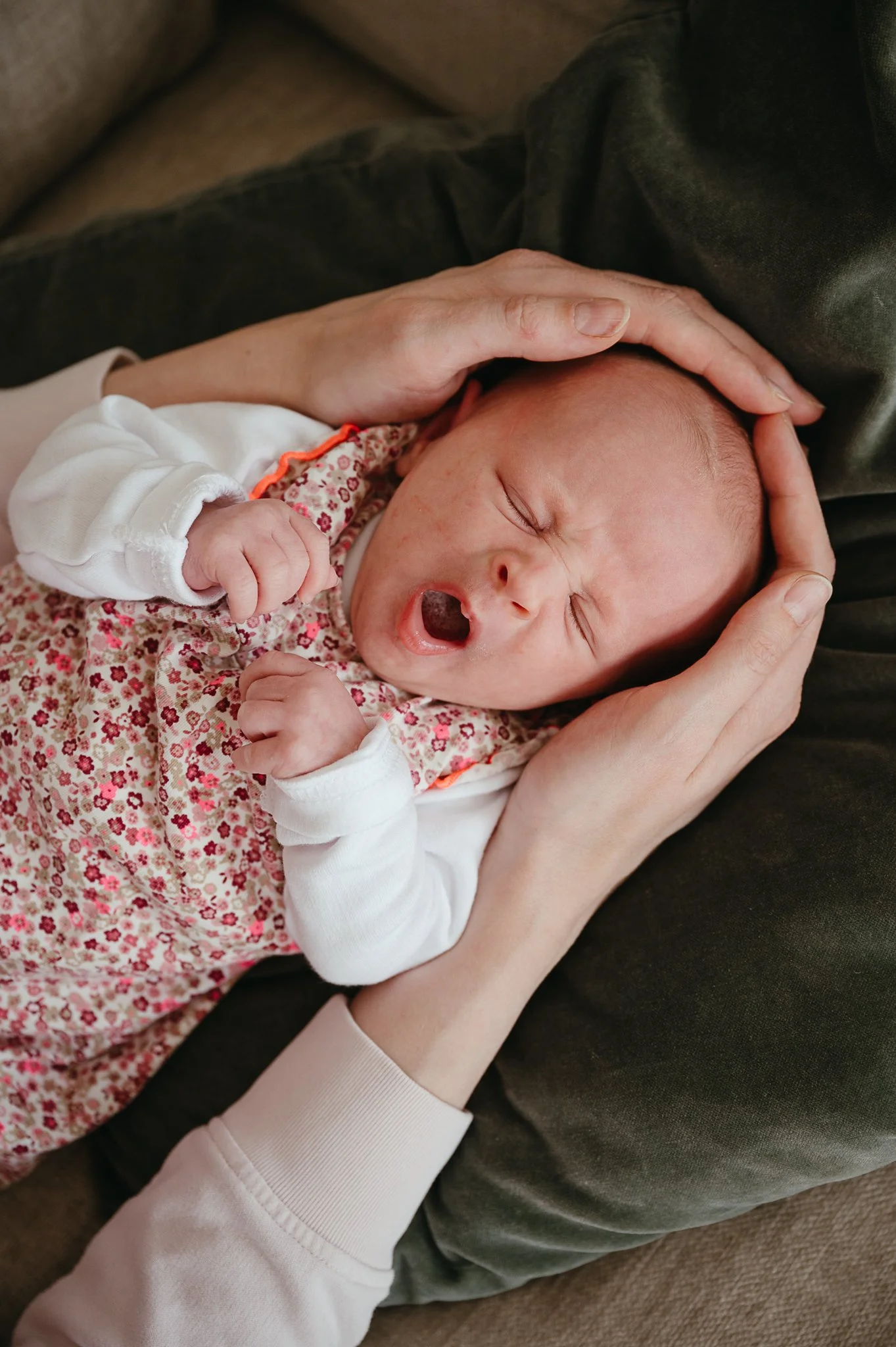 Ein gähnendes Baby, das in den Armen seiner Mutter liegt.