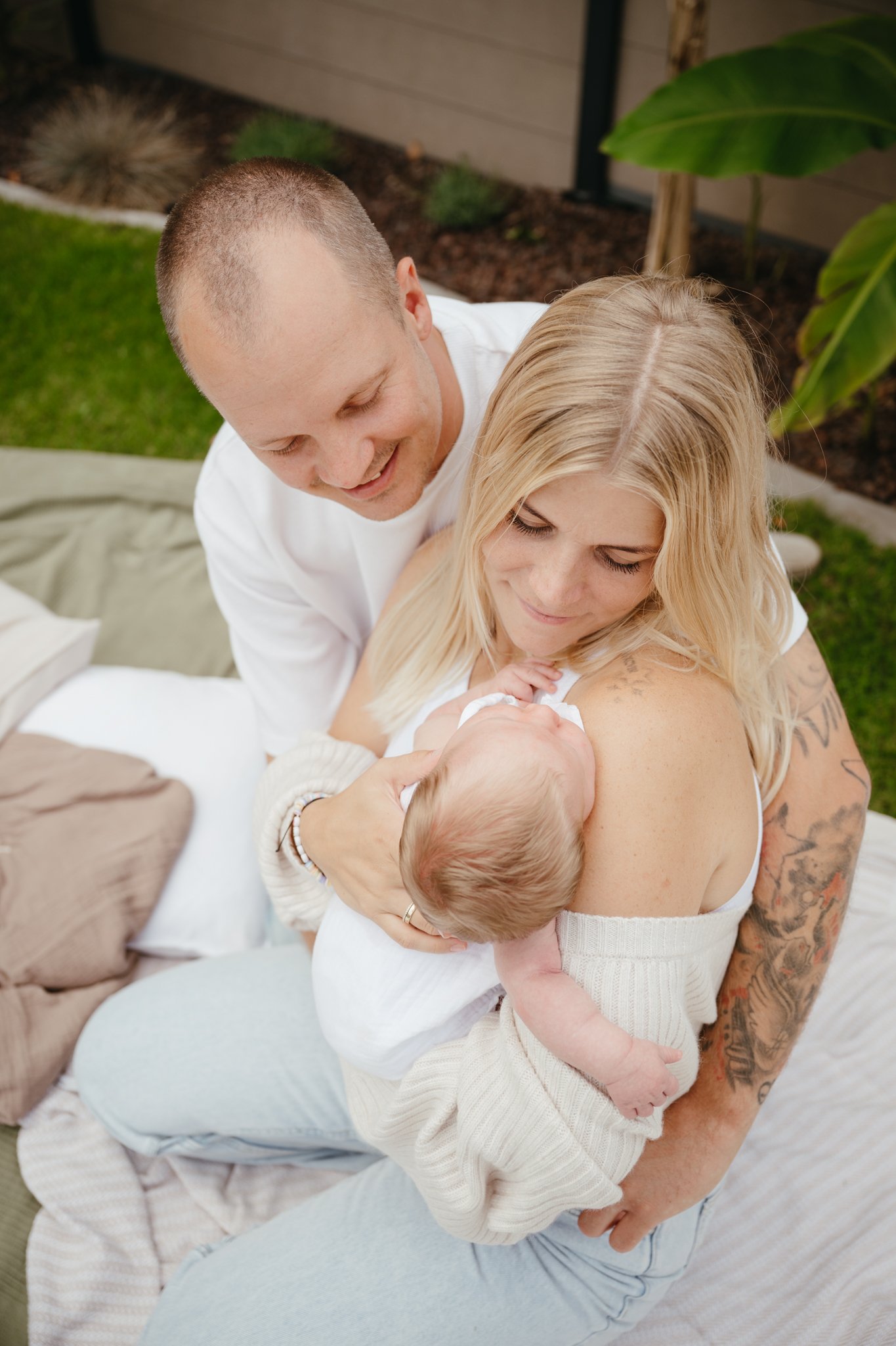 Eine glückliche Familie beim Kuscheln draußen im Garten, die Mutter hält das neugeborene Baby, während der Vater liebevoll zuschaut.