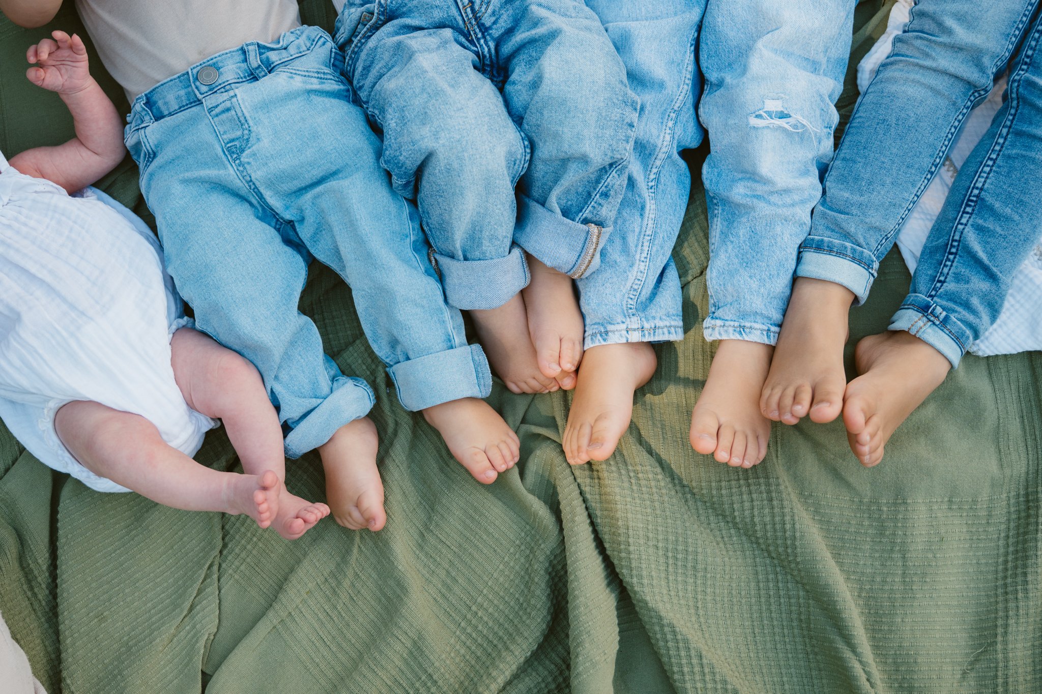 Mehrere Babys und Kinder in Jeans liegen nebeneinander auf einer grünen Decke.