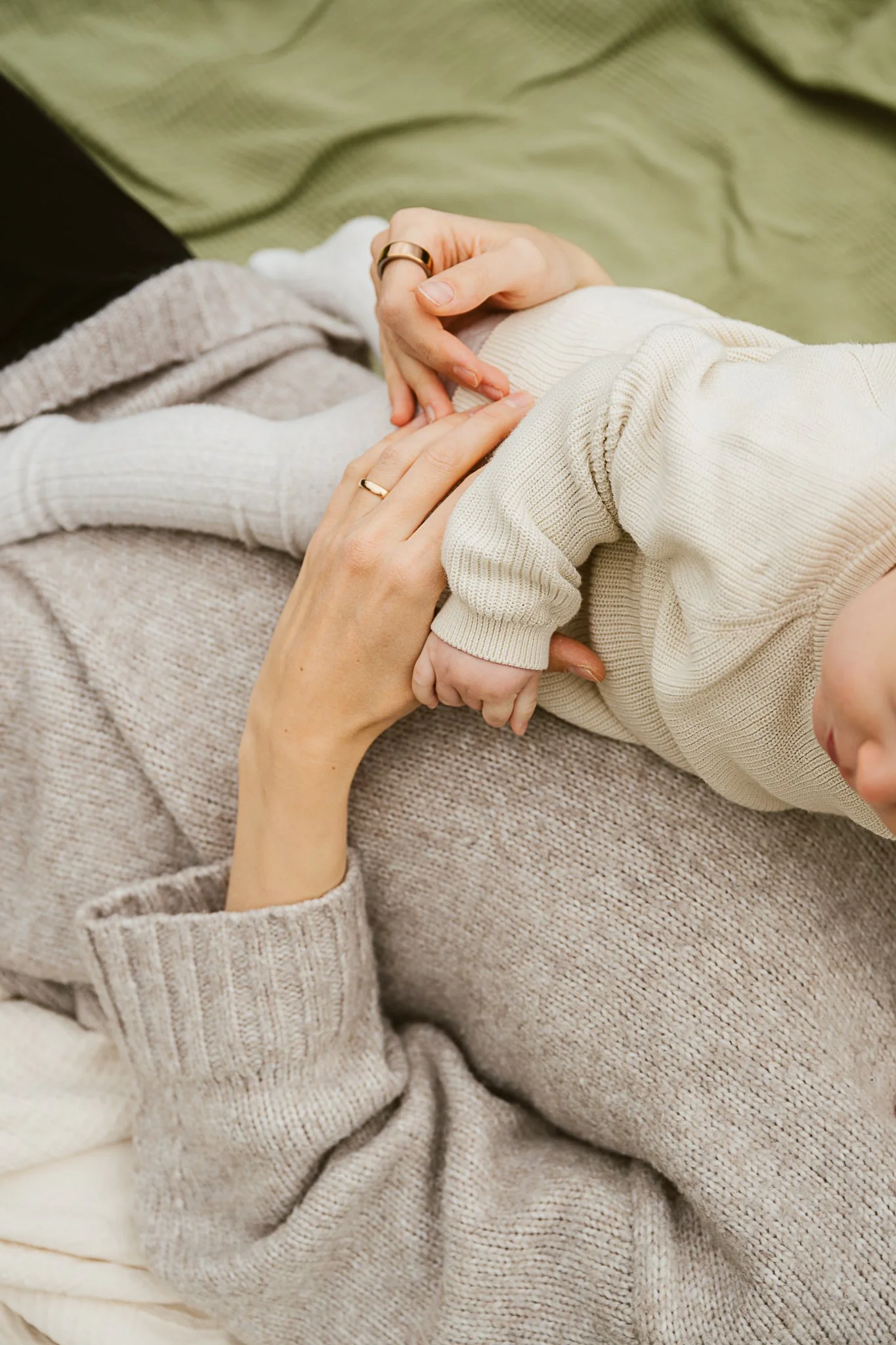 Nahaufnahme von einer jungen Frau, die einen kleinen Säugling auf dem Schoß hält, während sie auf einer grünen Decke liegt.
