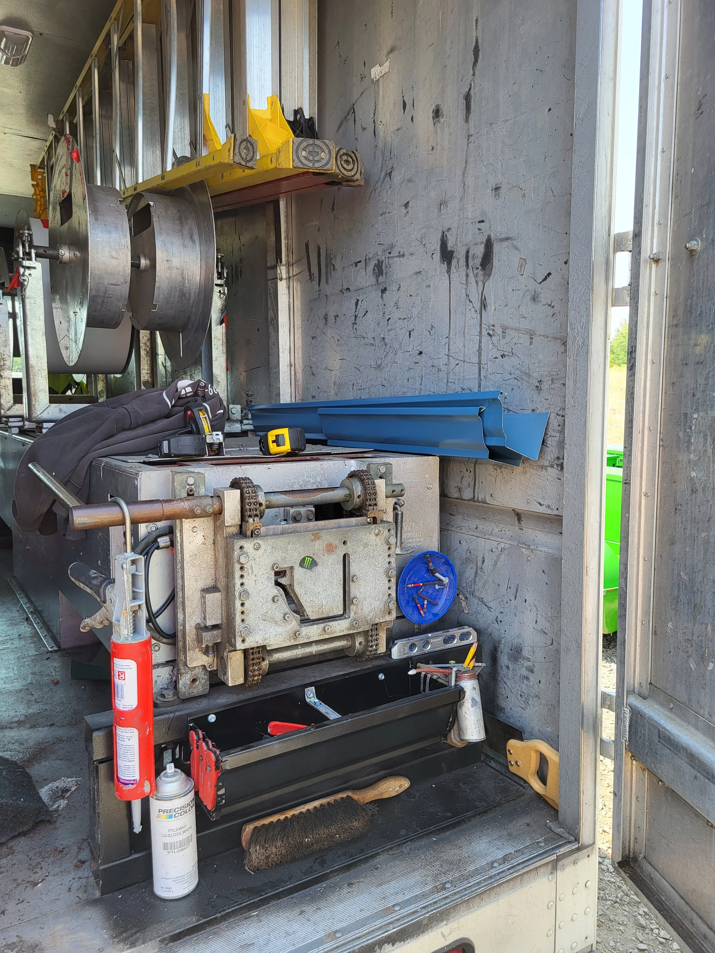 Tools and equipment inside a utility or service truck, including a fire extinguisher, a gauge, various metal components, a blue plastic part, and other tools on shelves and trays.