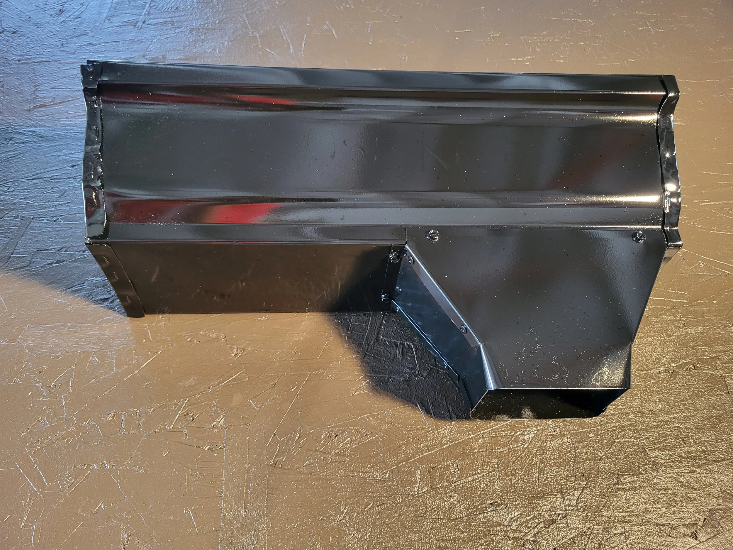 A black metal 6 inch gutter with an oversize outlet installed on it