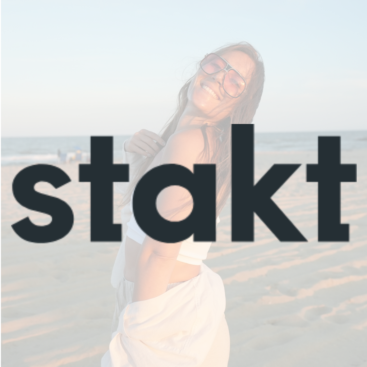 A woman smiling at the beach during sunset, wearing sunglasses and casual summer clothing.