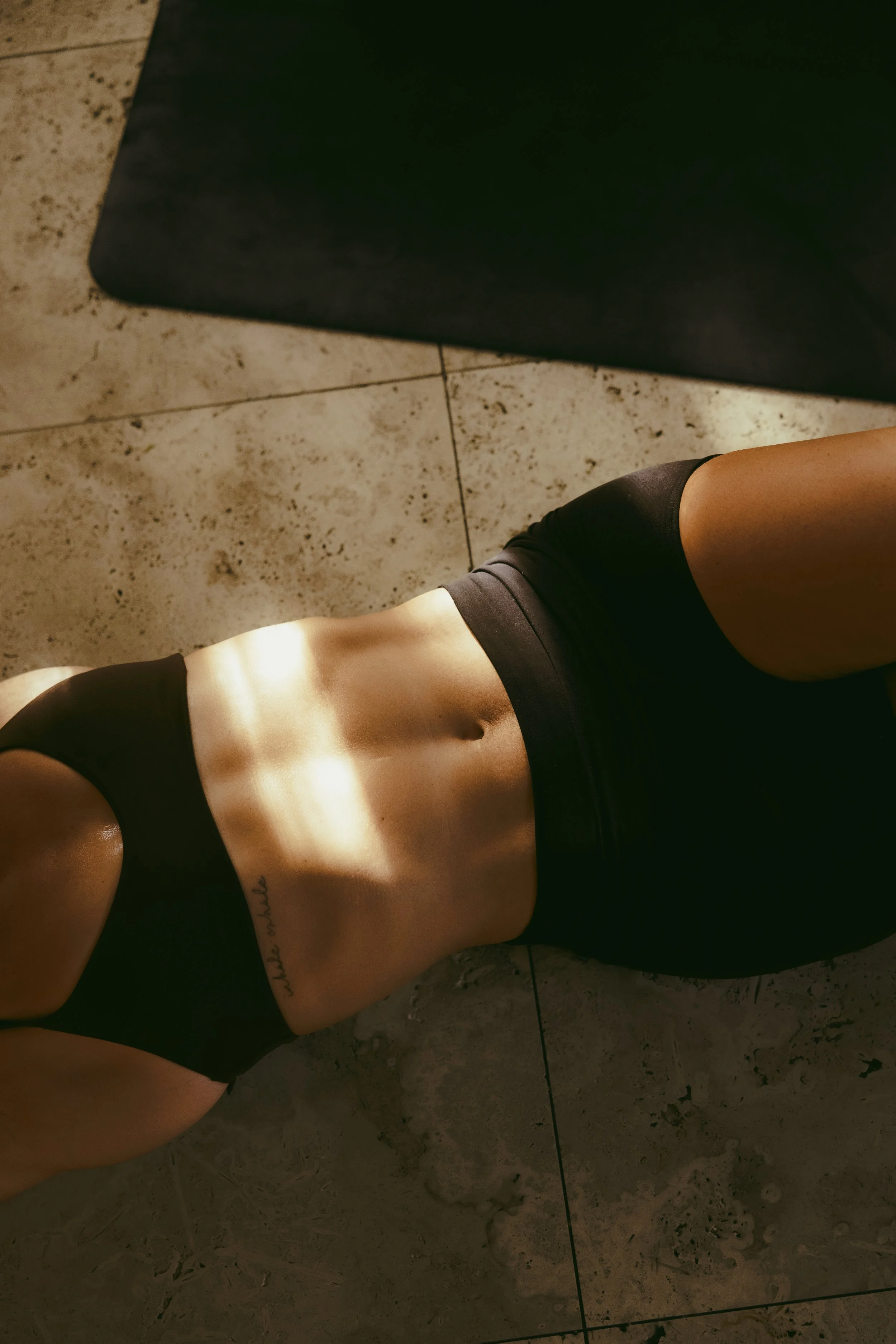 Abs of a fit woman laying on the floor in a matching black workout set