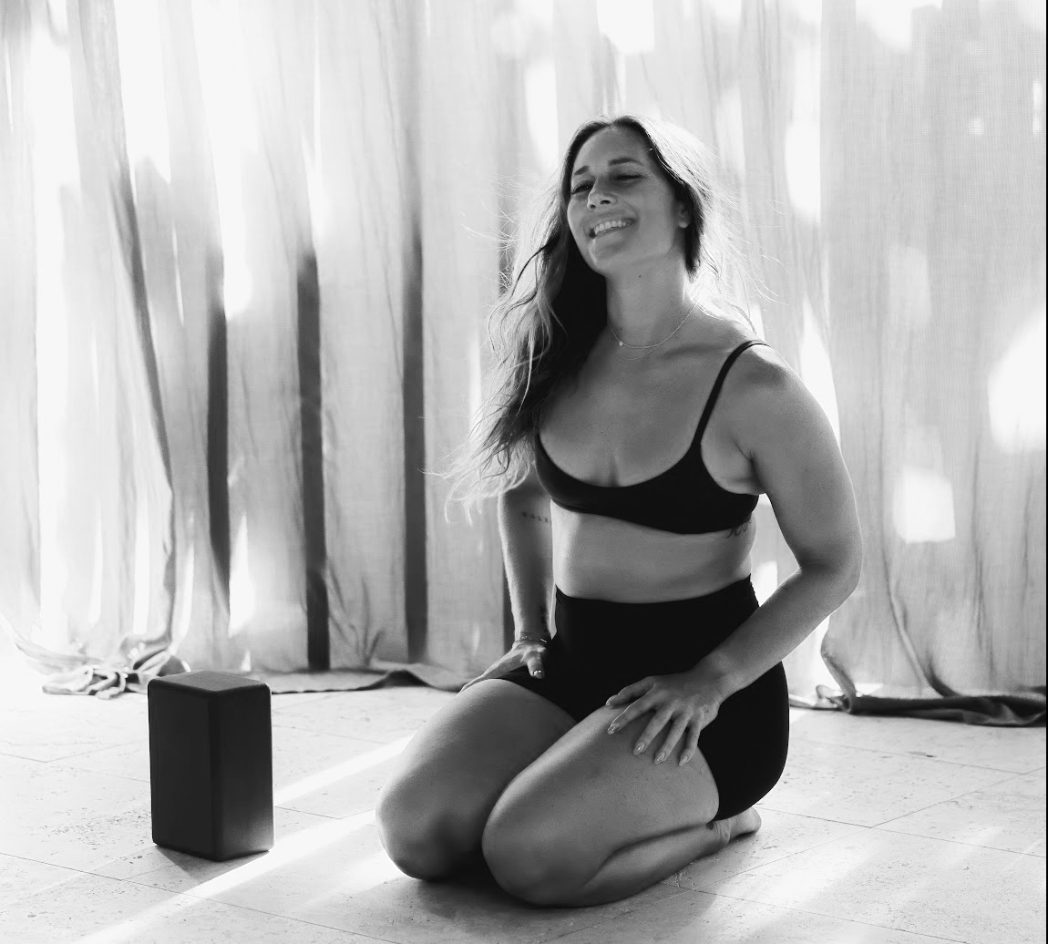 Beach scene in black and white with large leafy plants in the foreground, ocean waves, and a small island in the background under a cloudy sky.