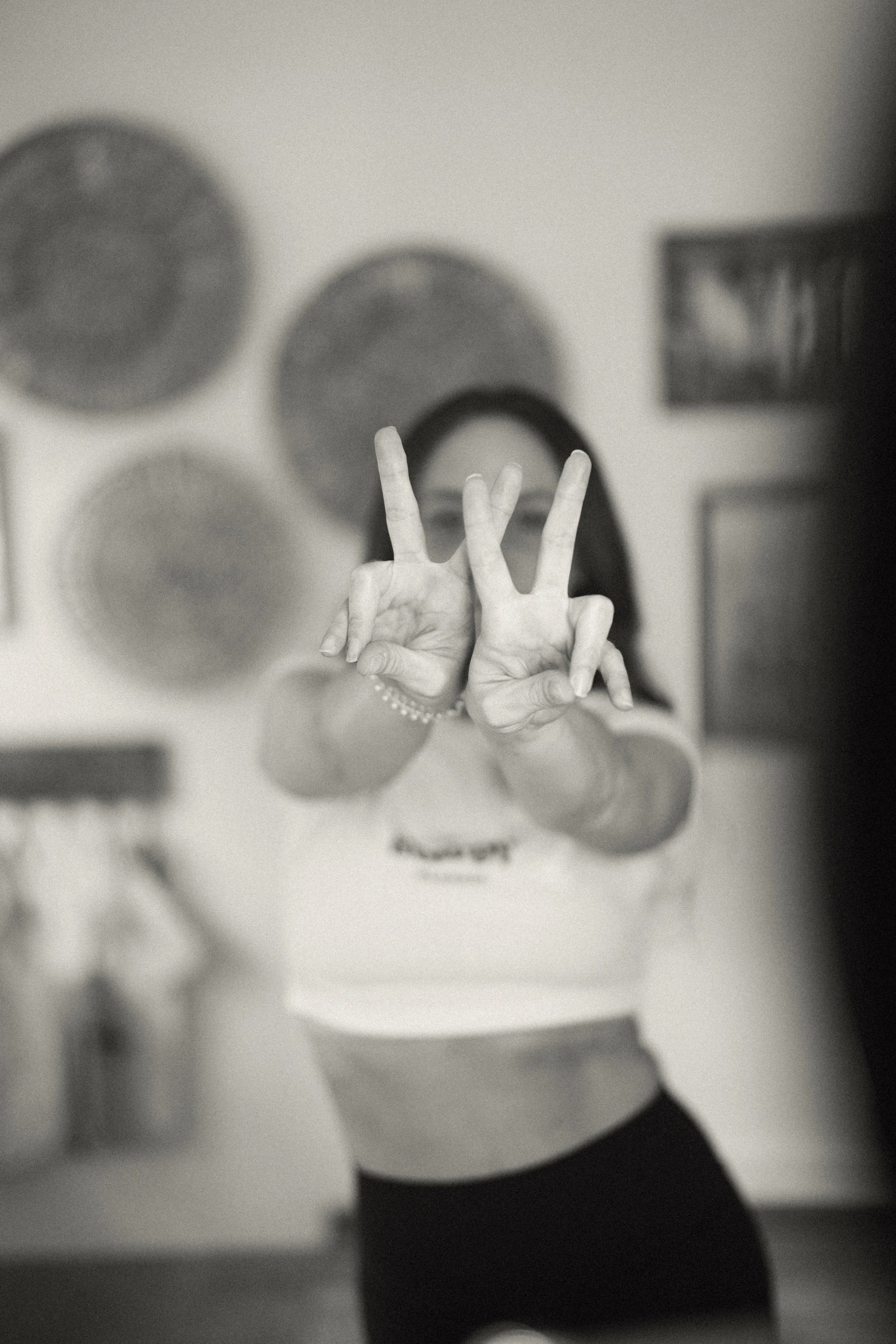 A girl with long hair taking a black and white mirror selfie, making a peace sign with her fingers.