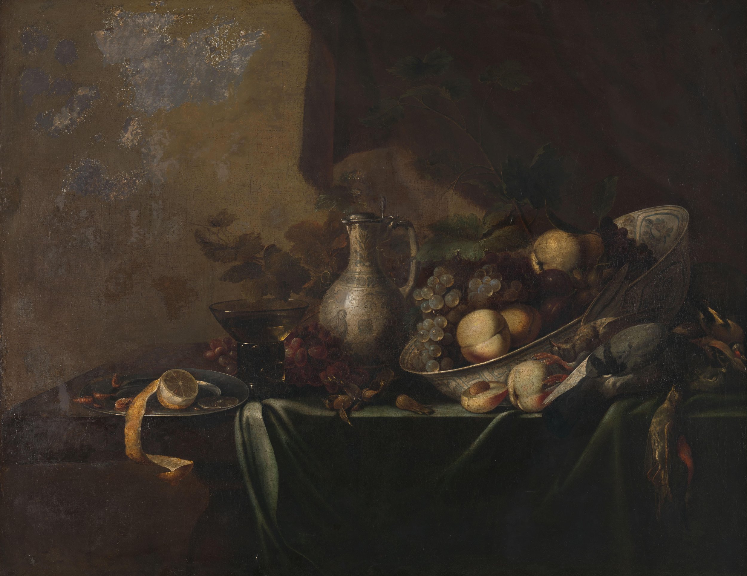 A dark still life painting featuring a parrot-shaped metallic vessel, various fruits including grapes, melons, lemons, and a pear, set on a table with a dark background.