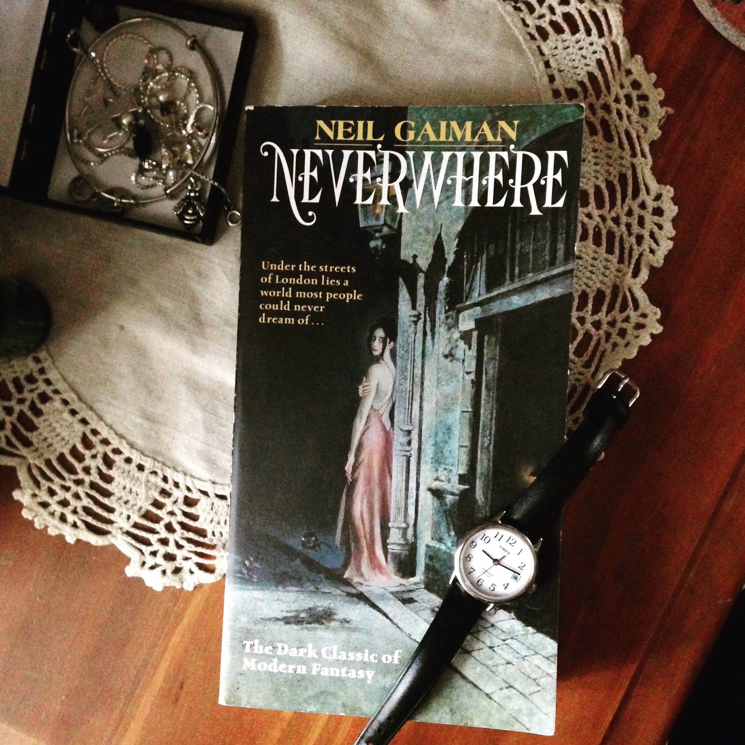 The book Neverwhere styled with a watch and box of jewelry on a wood surface