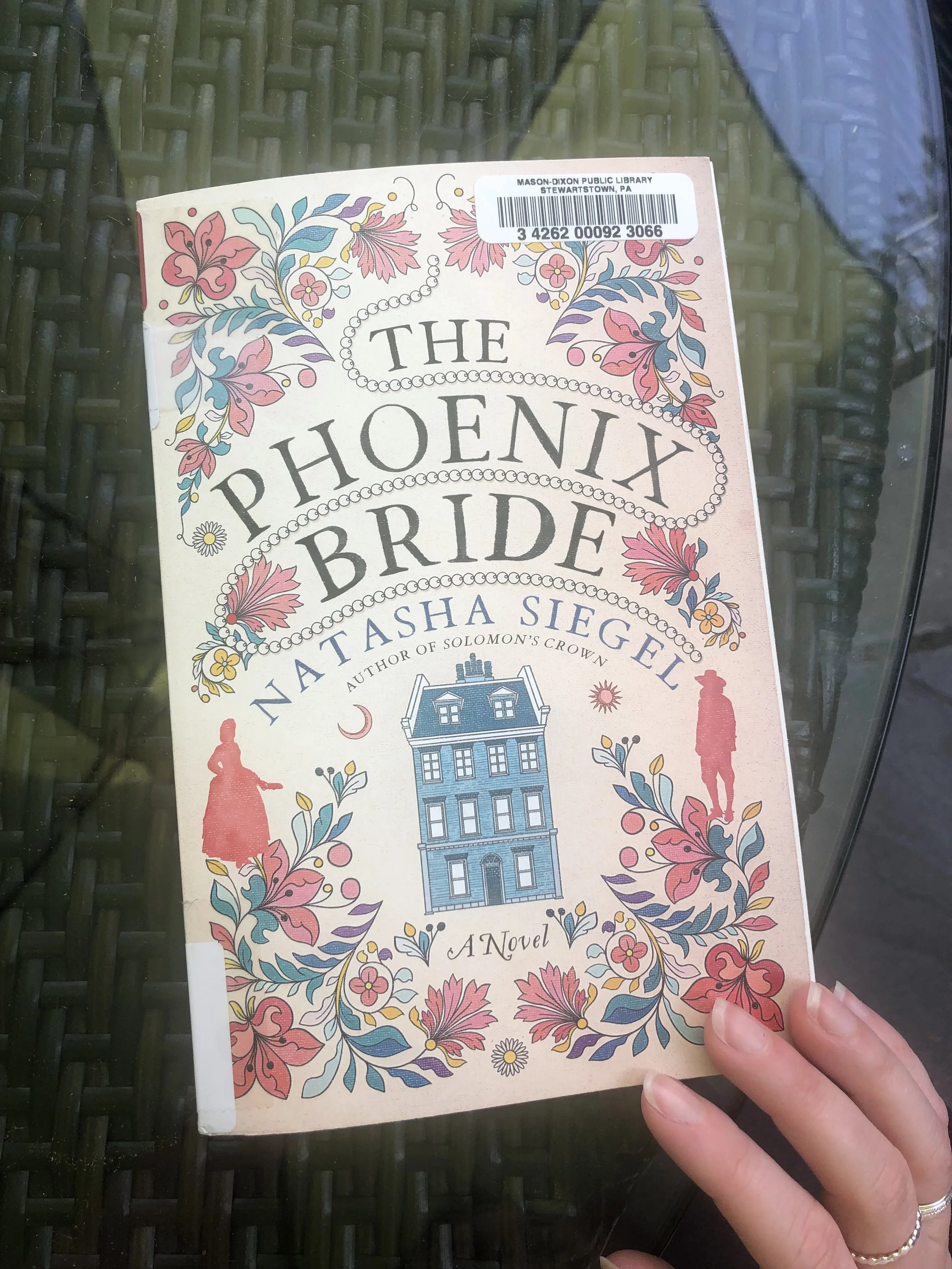 photo of the cover of The Phoenix Bride with a blue house and floral designs