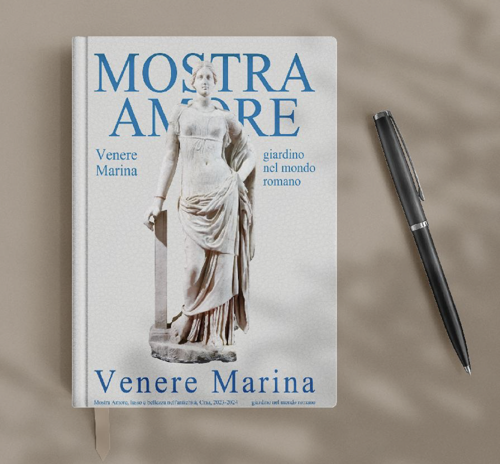 Book titled "Mostra Amore" by Venere Marina features a sculpture of a woman on the cover, placed on a neutral surface with a black pen beside it.