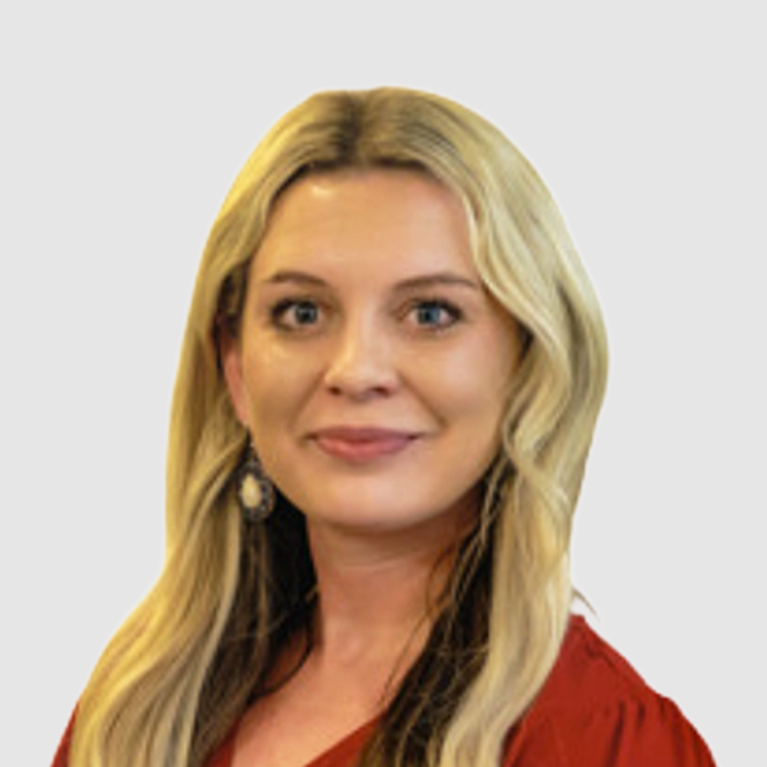 A woman with long, wavy blonde hair, wearing a red top and earrings, smiling against a white background.