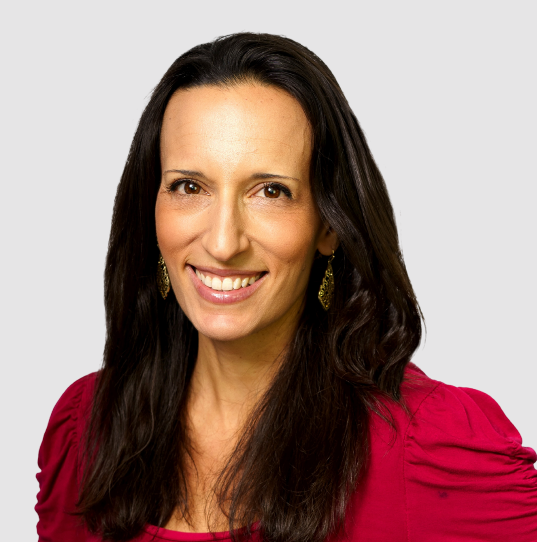A woman with long dark hair wearing a red top and gold earrings, smiling at the camera.