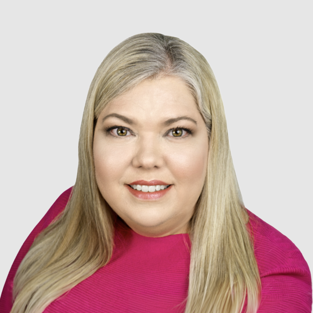 A woman with long blonde hair, wearing a bright pink top, smiling at the camera against a white background.