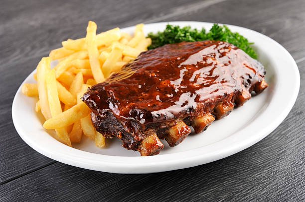 Barbecue ribs with coleslaw, French fries, and chicken wings on a white oval plate.