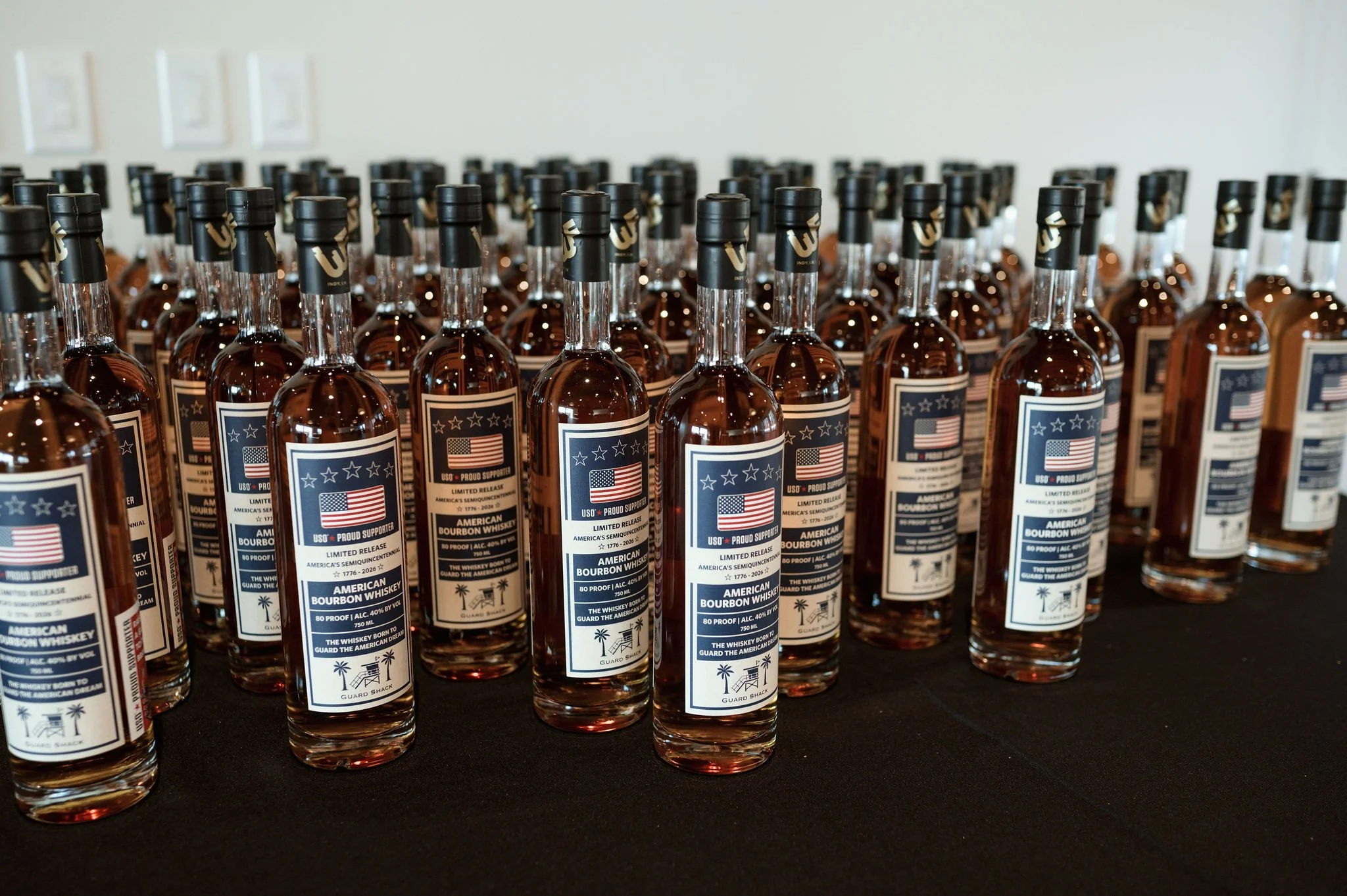 Rows of bottled American bourbon whiskey on a black surface, with labels featuring American flags and palm trees.