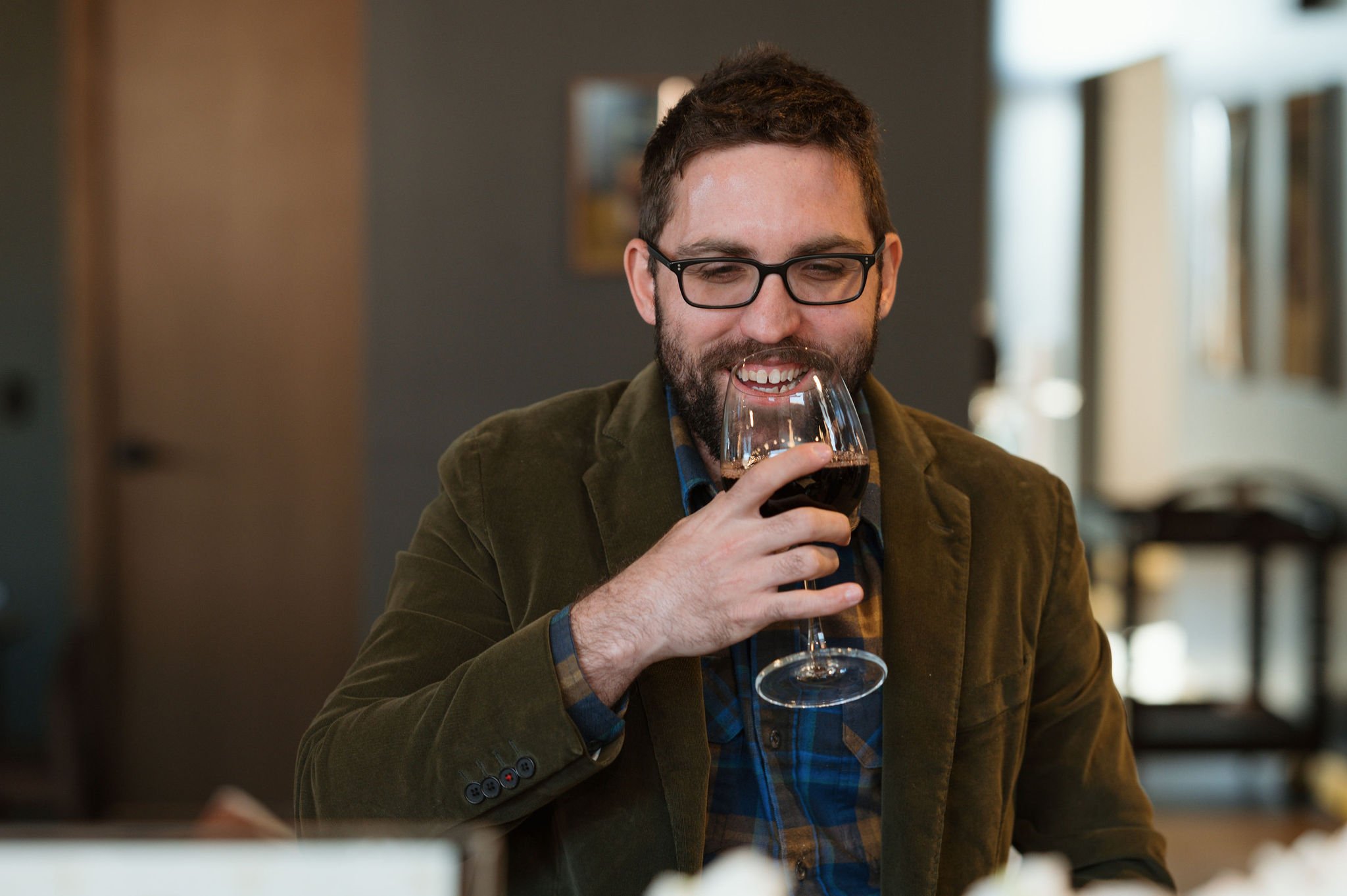 Man with glasses smiling as he smells a glass of red wine