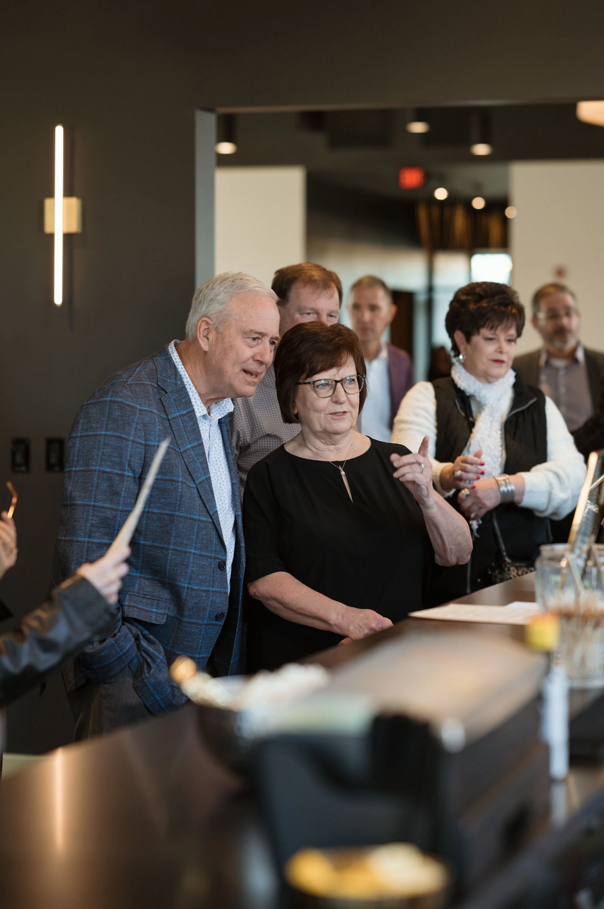 A group of people gathered around a counter, engaged in conversation or a discussion at what appears to be a social or professional event, in a modern, well-lit space.