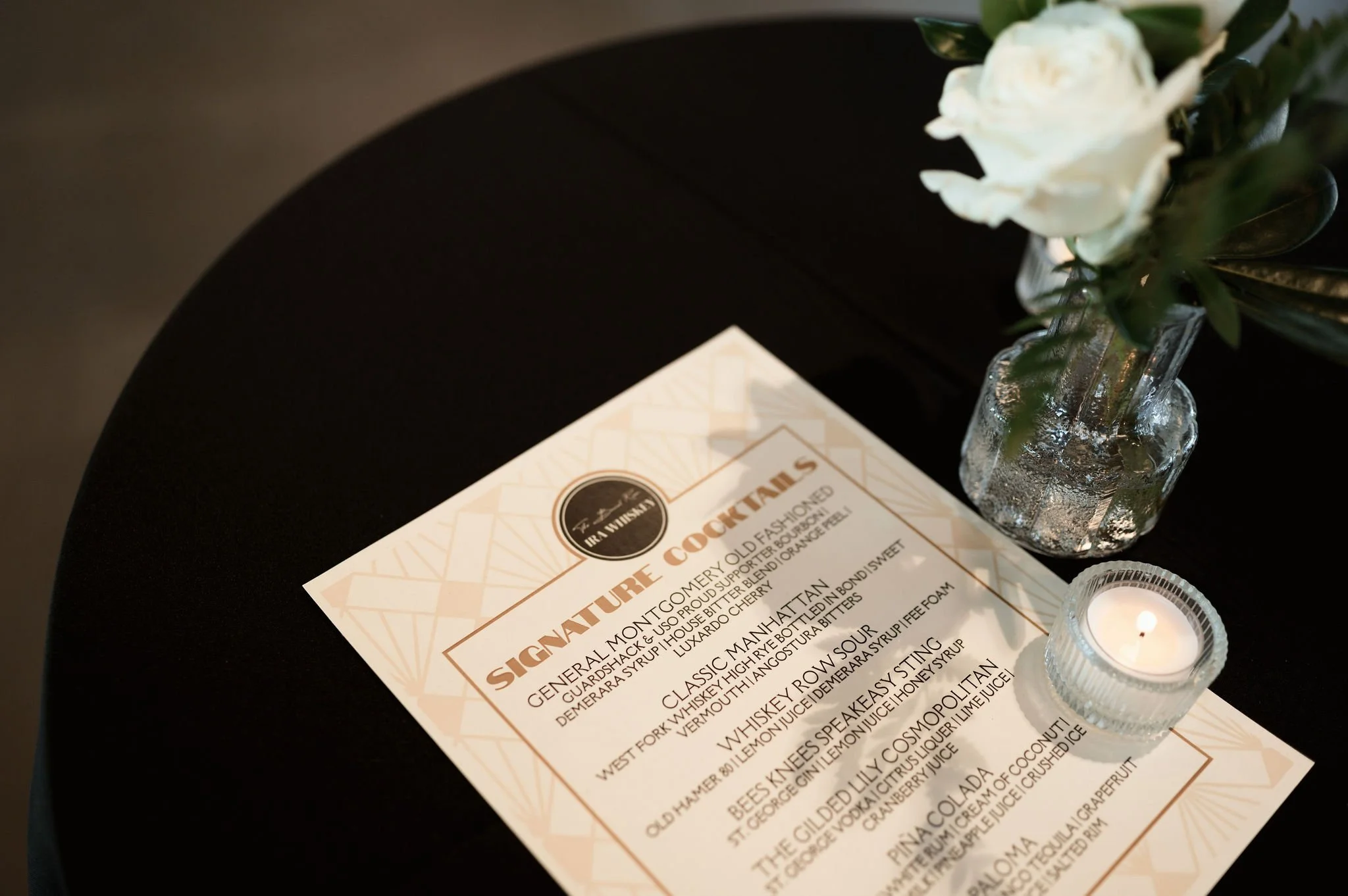 A black table with a menu, a glass vase with white flowers, and a small candle