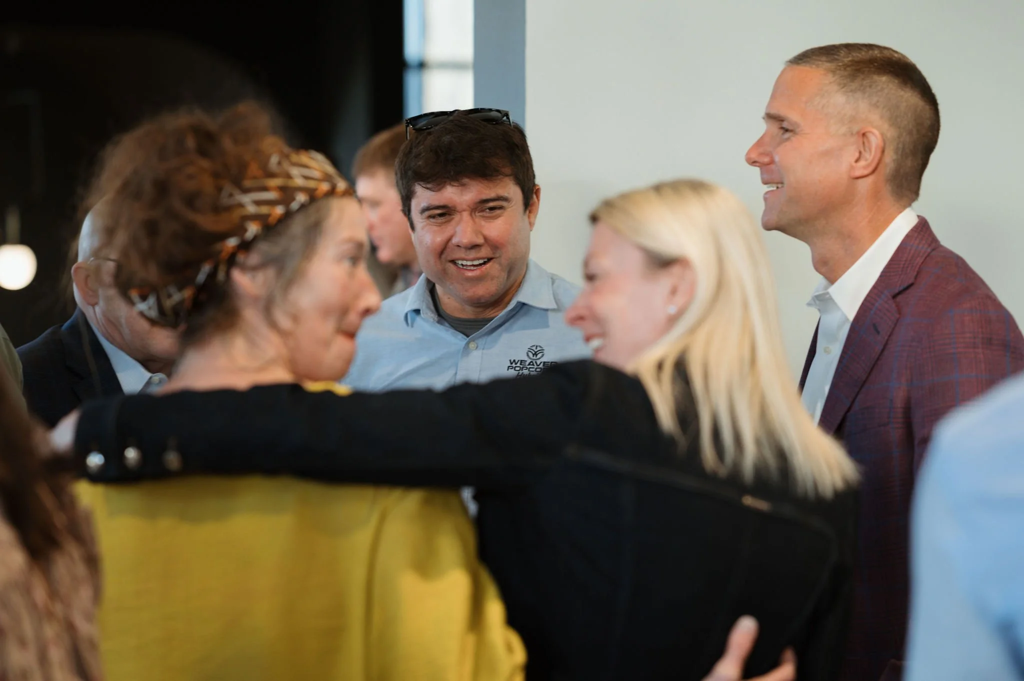 Group of people engaged in conversation at an indoor event, including men and women of various ages.
