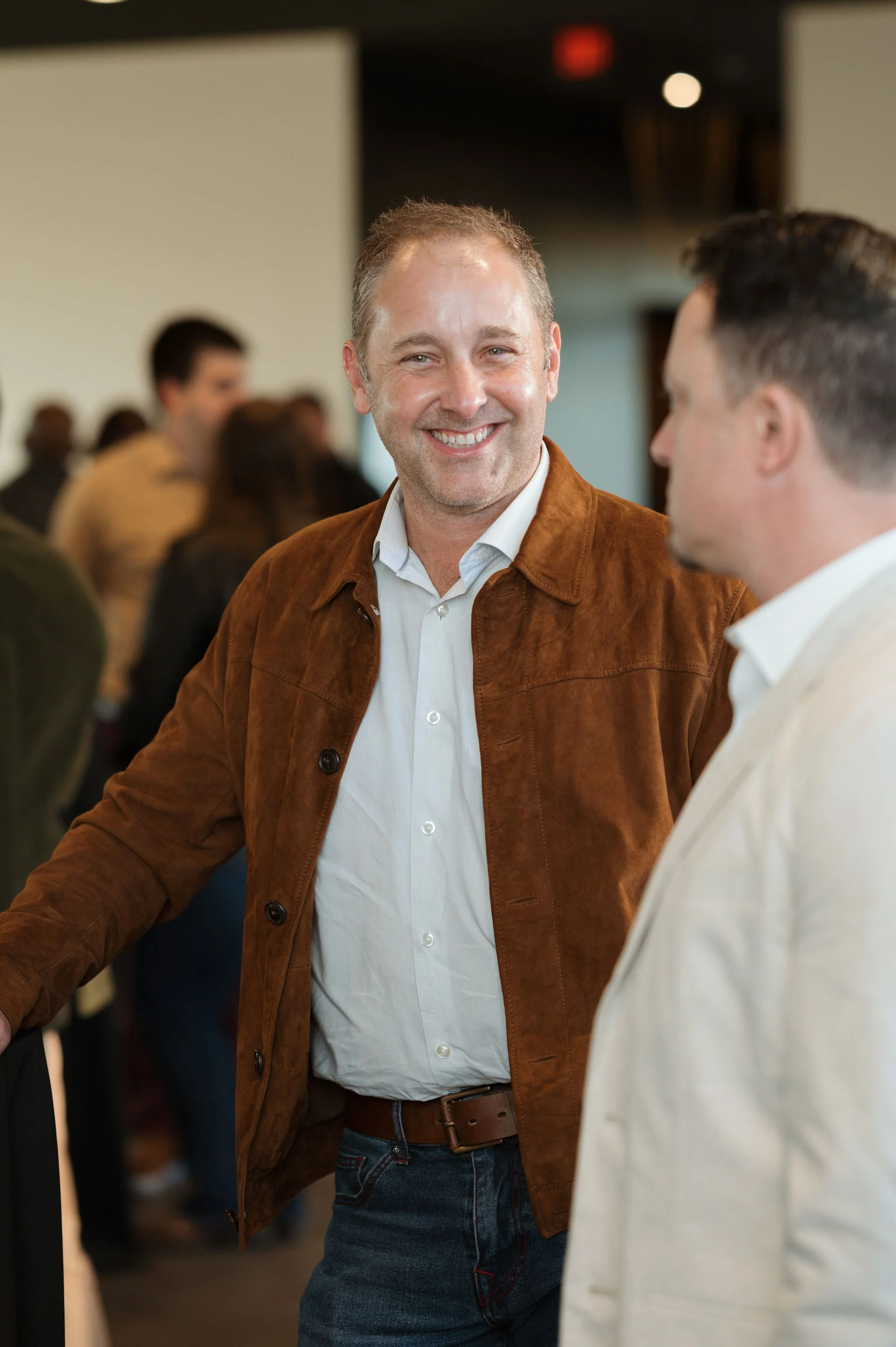 Two men engaging in conversation at a social gathering, with people in the background.