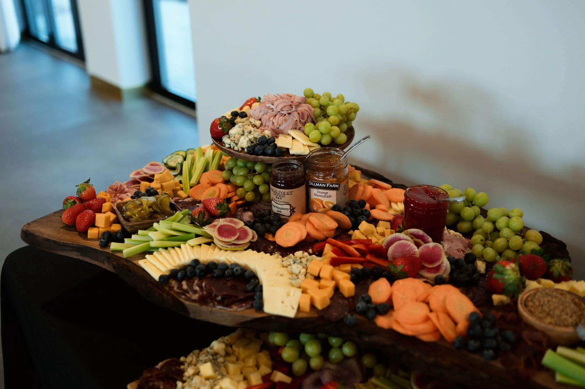 A charcuterie board with various cheeses, fruits, vegetables, jams, and crackers.