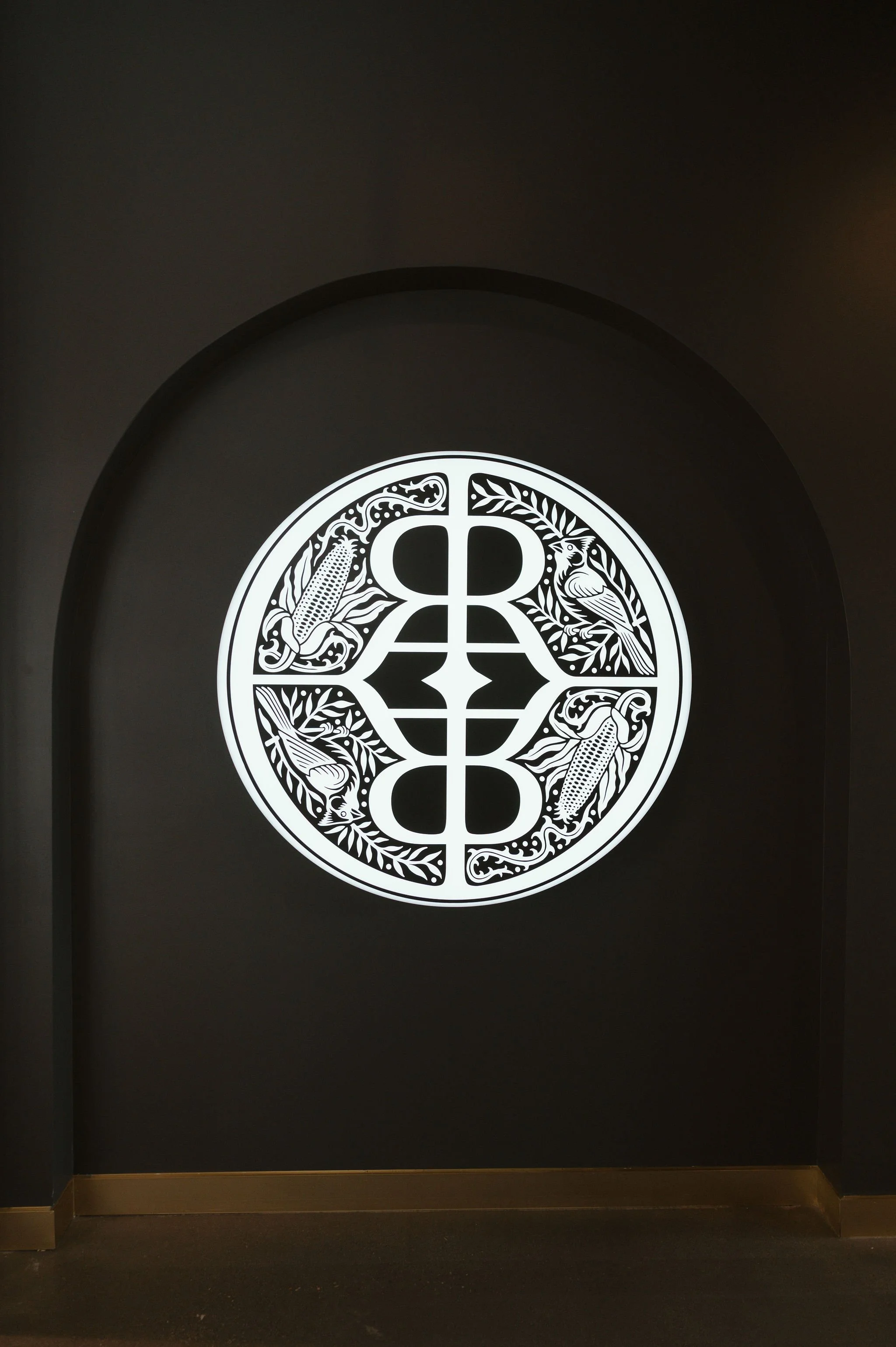 Decorative black circle with white intricate patterns including birds, corn, and leaves, on a black background.