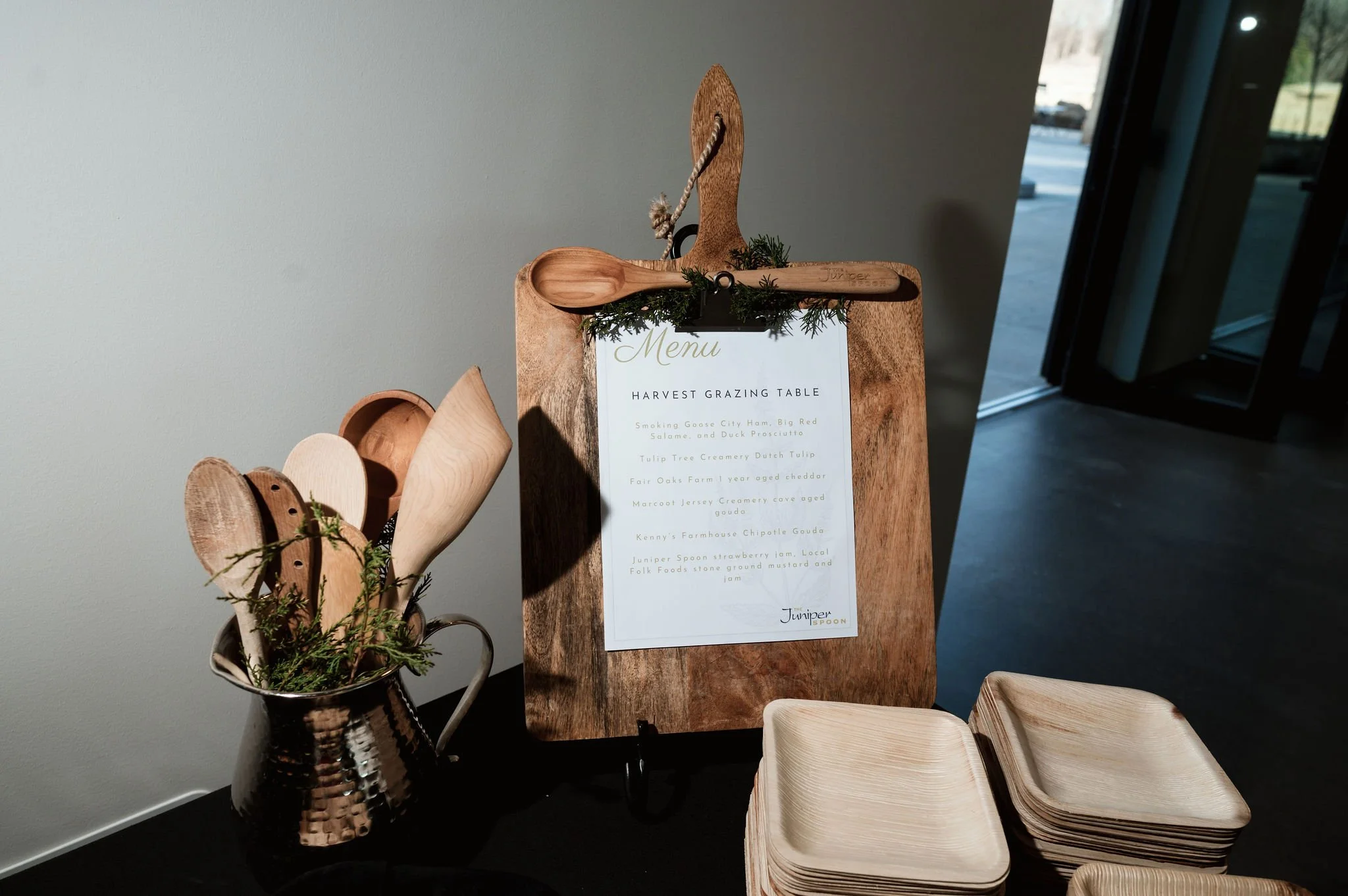 Wooden cutlery and plates on display with a menu sign for a harvest grazing table at a restaurant or event.