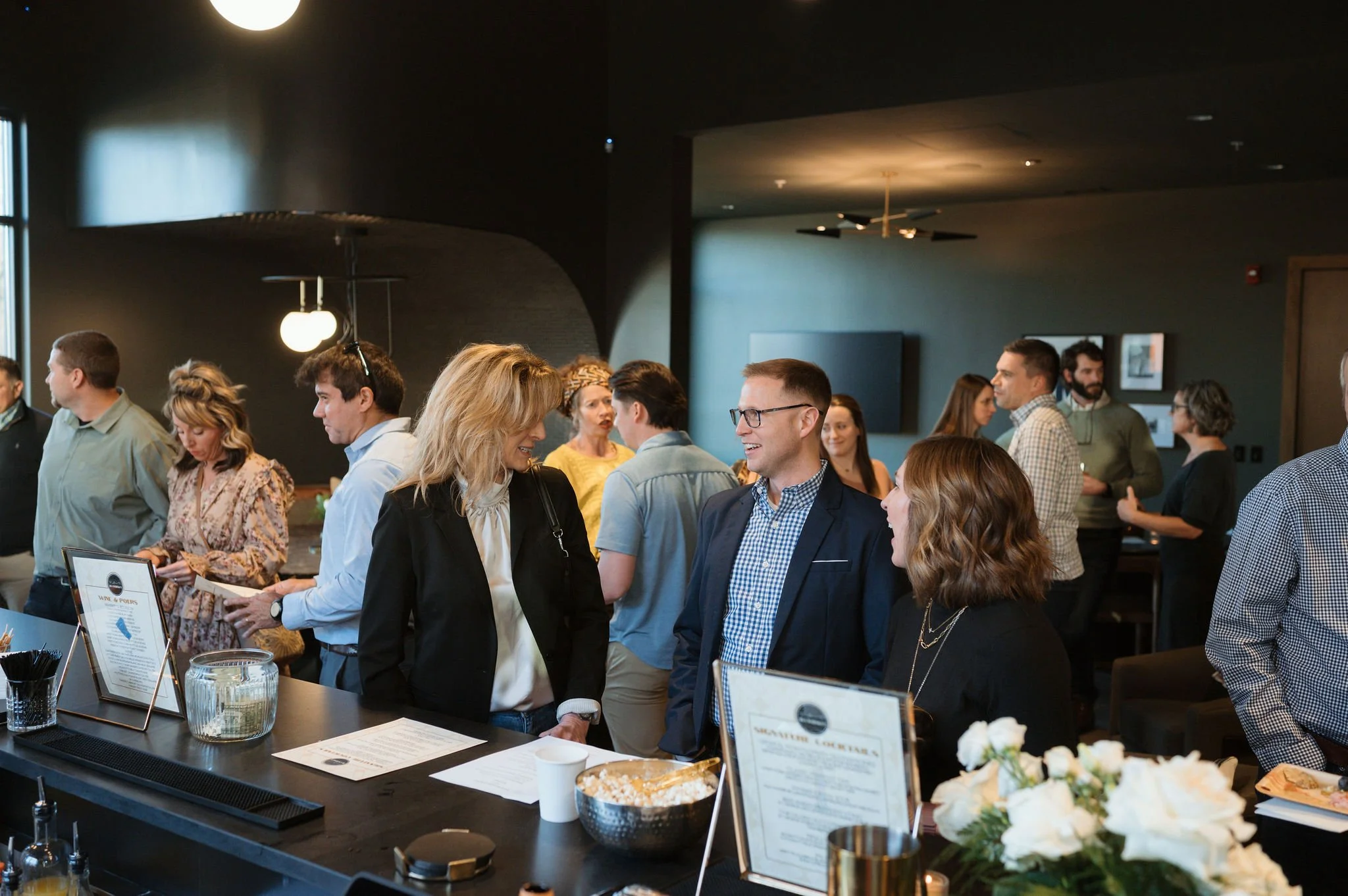 People socializing and ordering at a bar or cafe in a modern indoor setting with dark walls and contemporary decor.