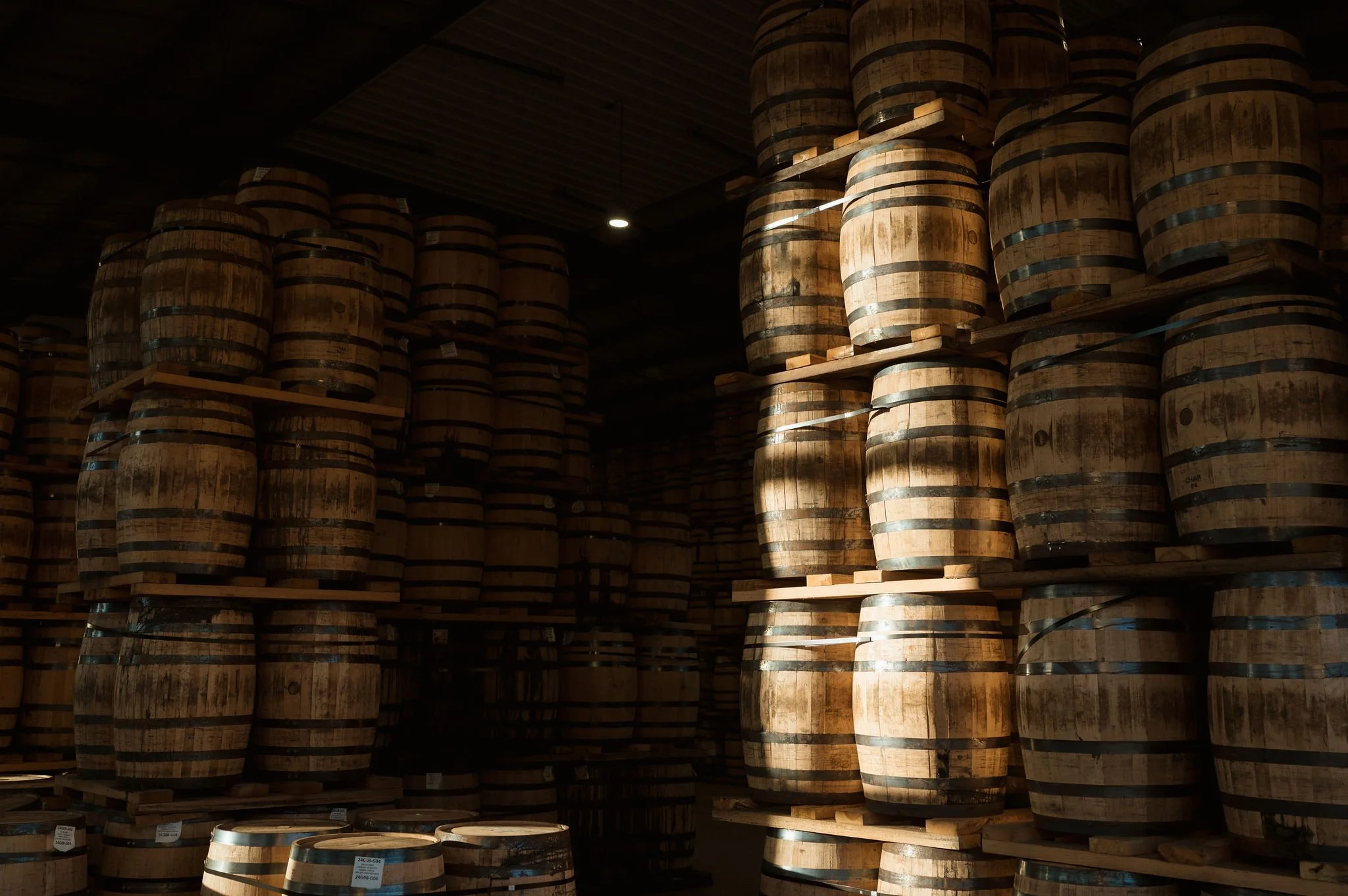 Stacks of wooden barrels stored in a warehouse with low lighting and wooden ceiling