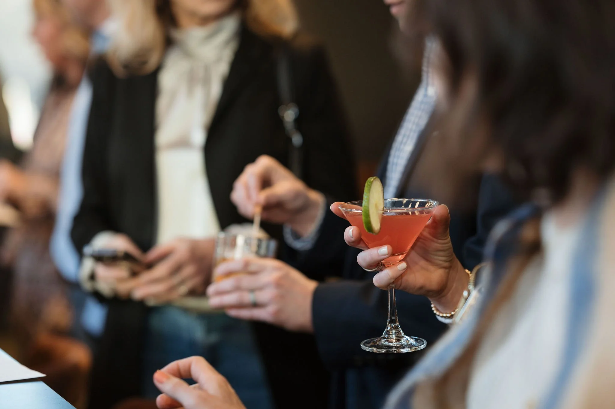 A woman holding a pink cocktail garnished with a lime wedge at a social gathering.